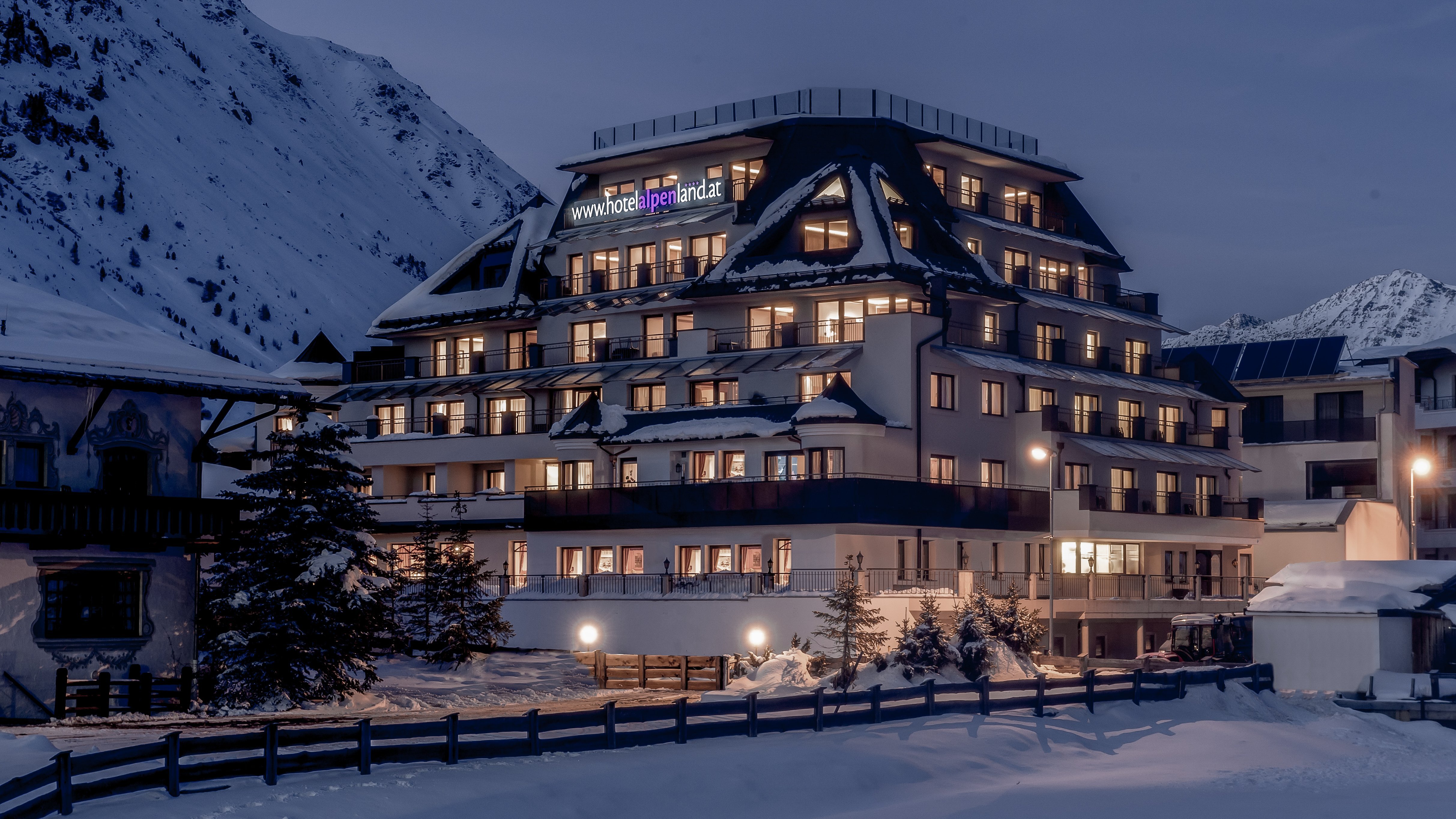 Mehrstöckiges Hotelgebäude in einer verschneiten Berglandschaft bei Dämmerung.