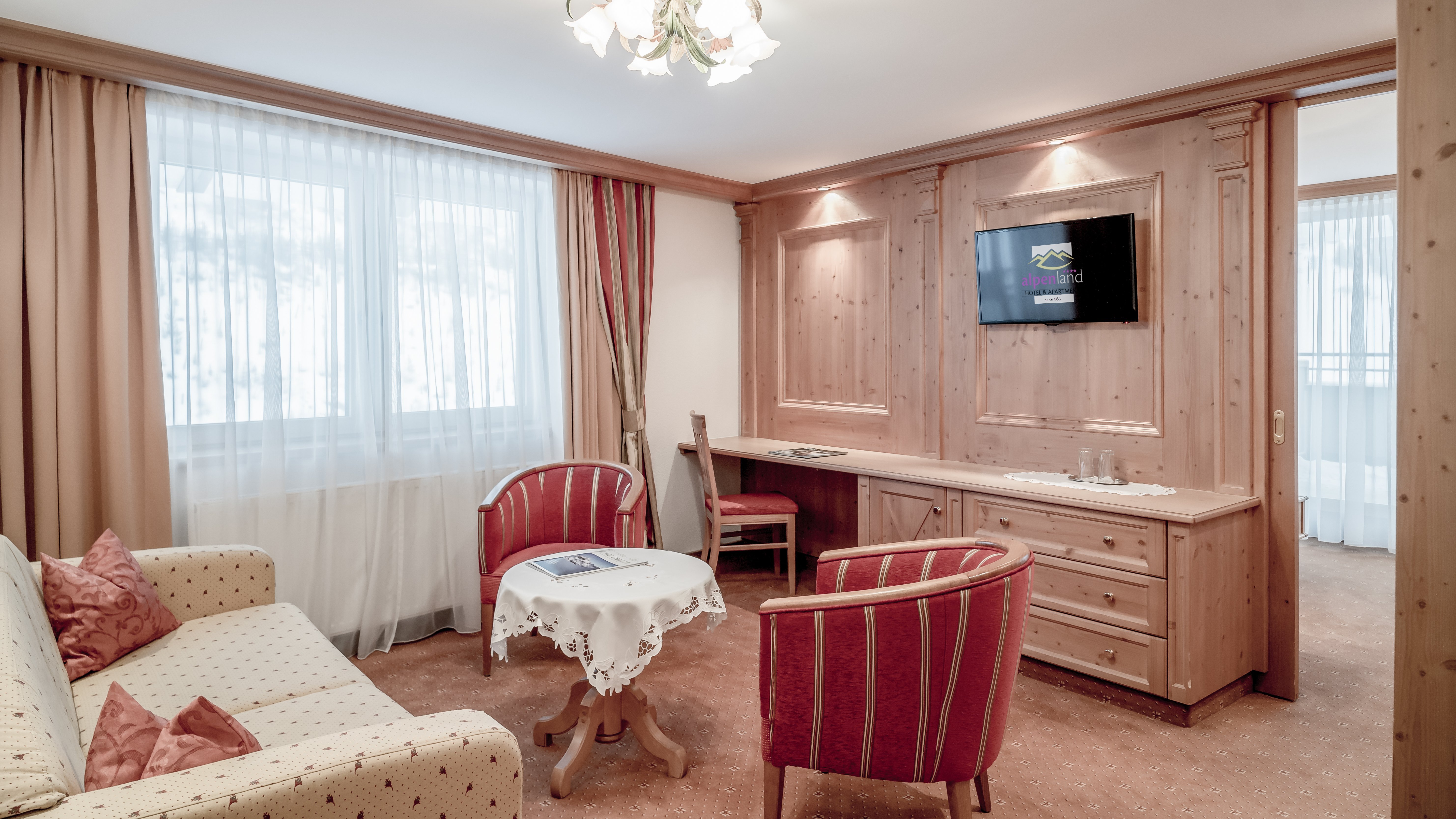 Gemütlicher Wohnraum im Alpenland Hotelzimmer mit Holzverkleidung, Sofa und Sesseln sowie Fernseher an der Wand gesehen.