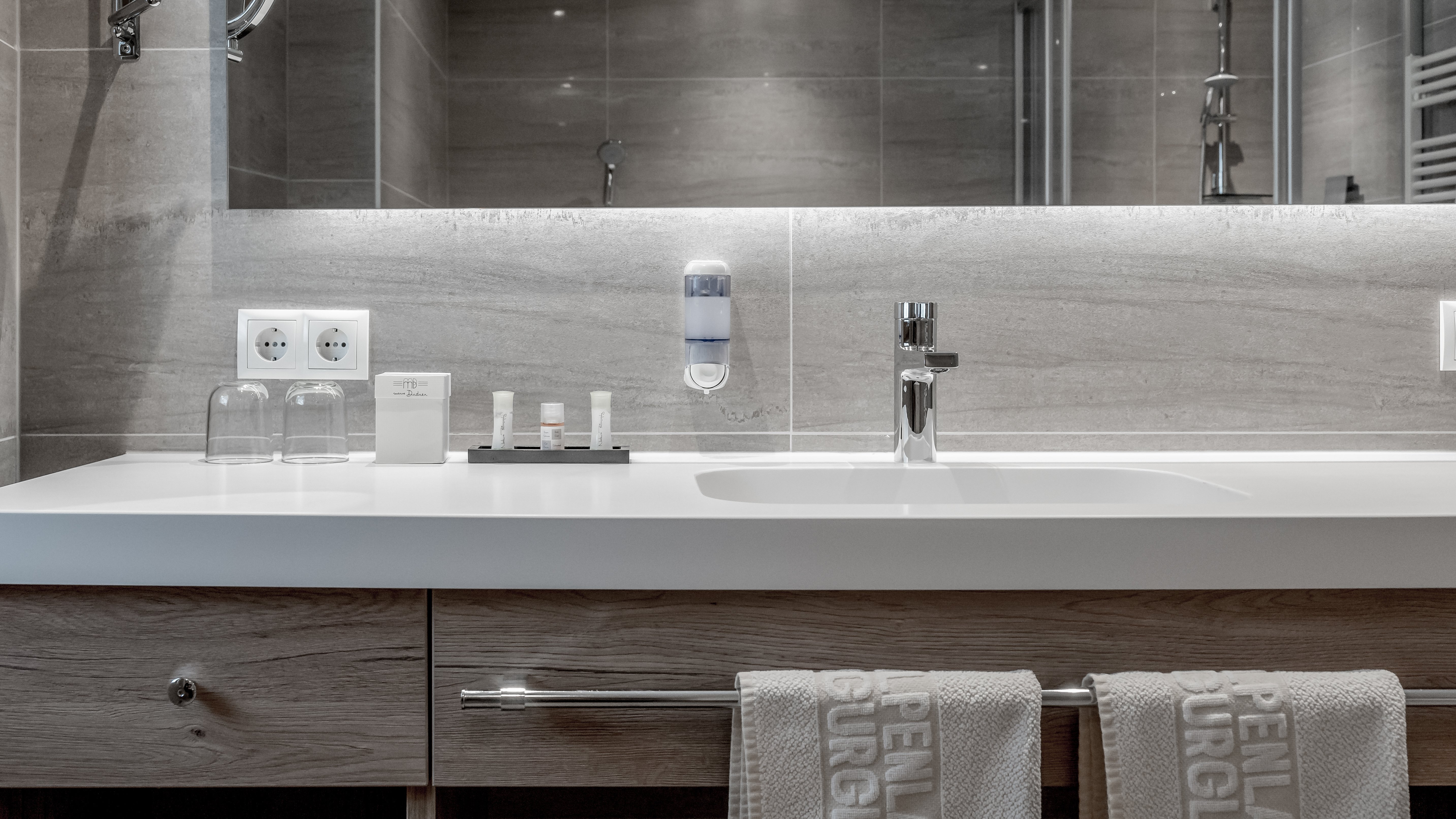 Moderne Badezimmergestaltung im Alpenland Badezimmer mit modernem Waschbecken, Spiegel und dekorierten Toilettenartikeln in geordneter Anordnung.