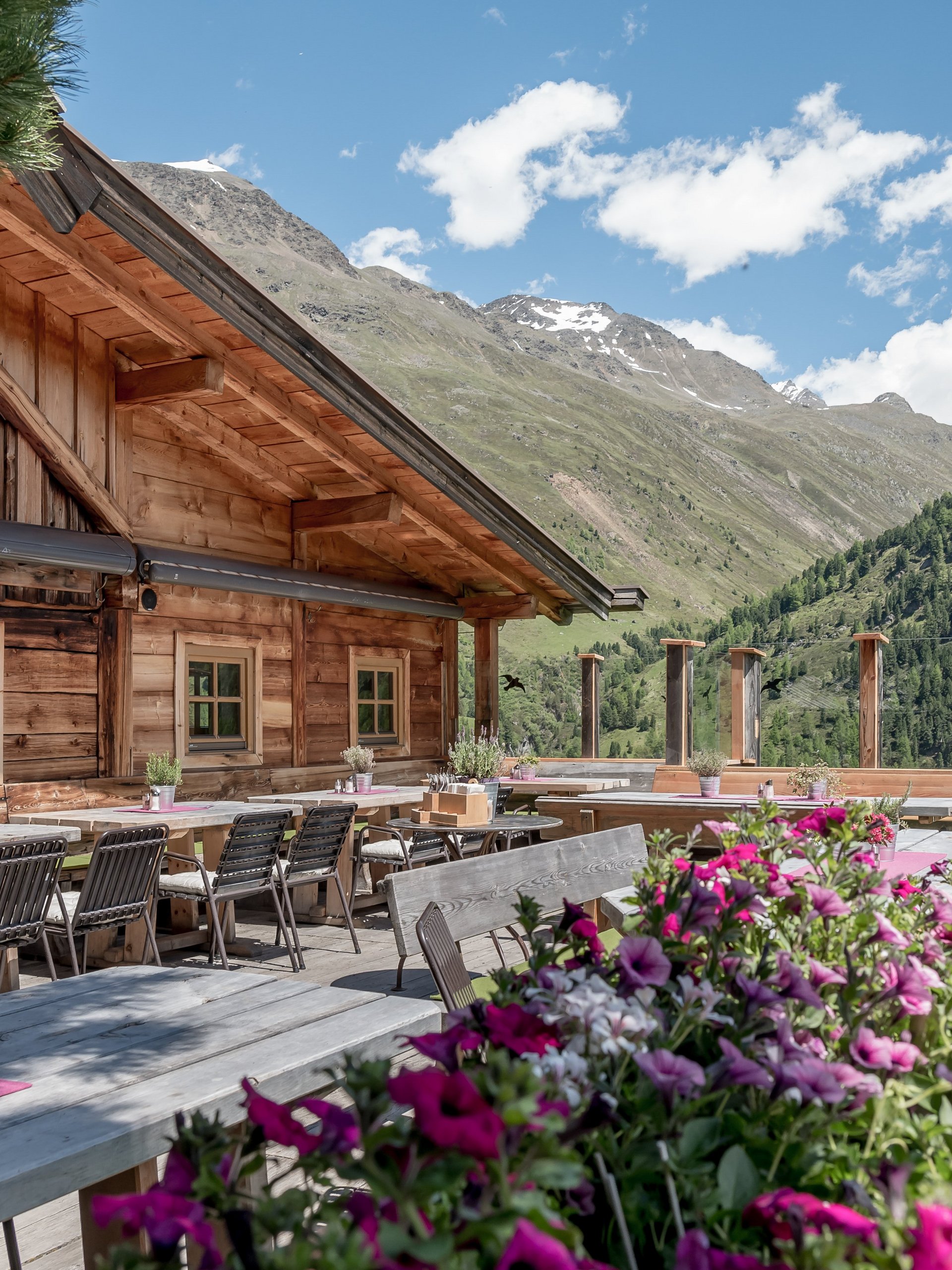 Außenansicht eines Bergrestaurants mit Blumen und Bergblick zur Sommersonne hin.