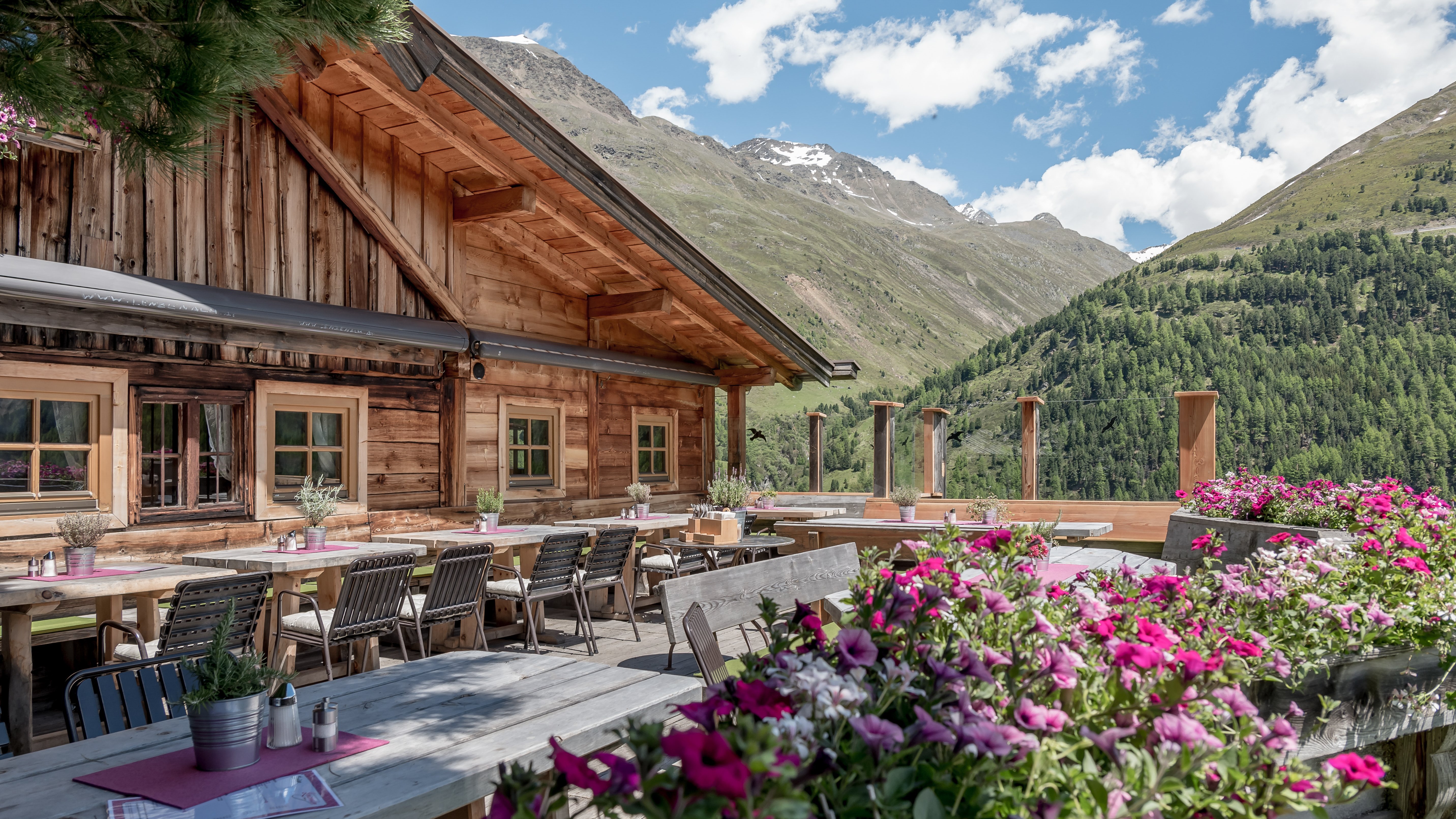 Bergrestaurant mit Holzarchitektur Außenansicht eines Bergrestaurants mit Blumen und Bergblick zur Sommersonne hin.