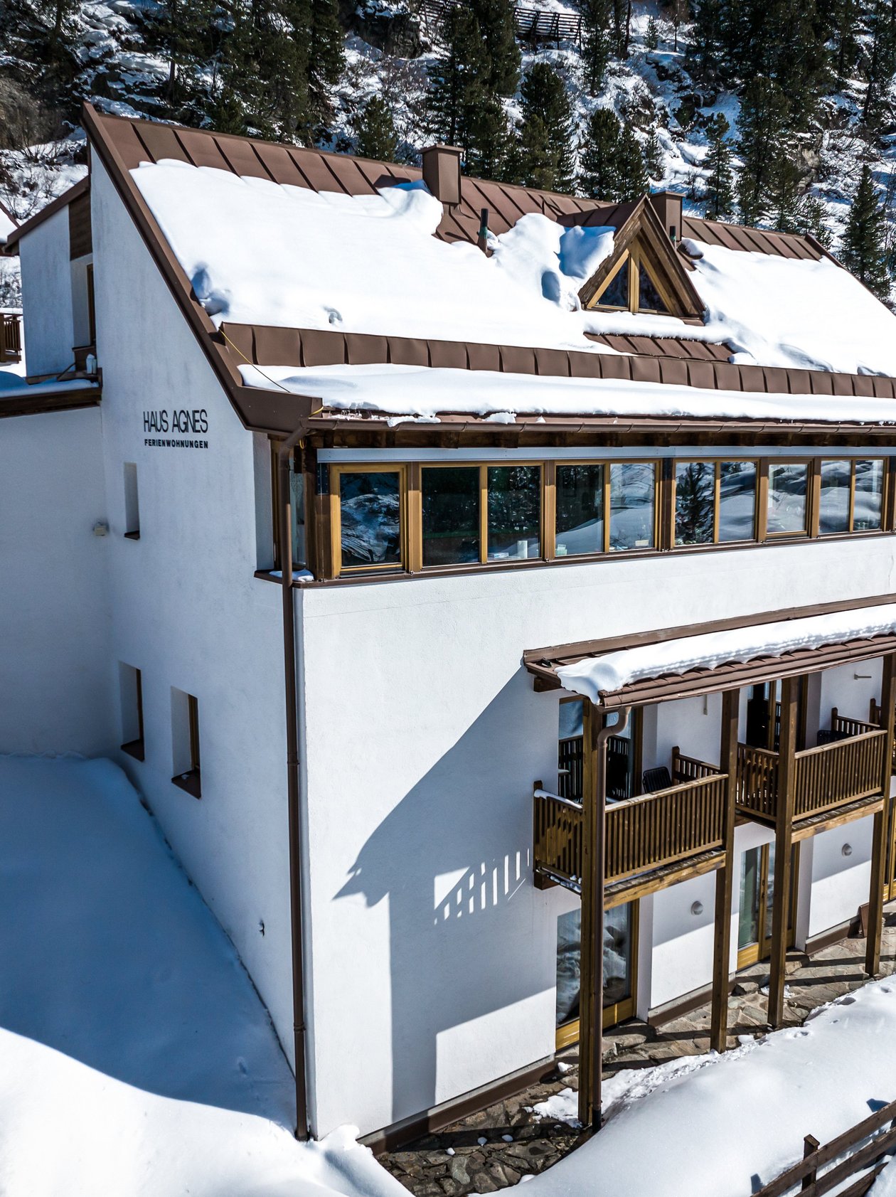 Schneebedecktes Bergchalet in einer winterlichen Landschaft mit Holzbalustraden und großen Fenstern.
