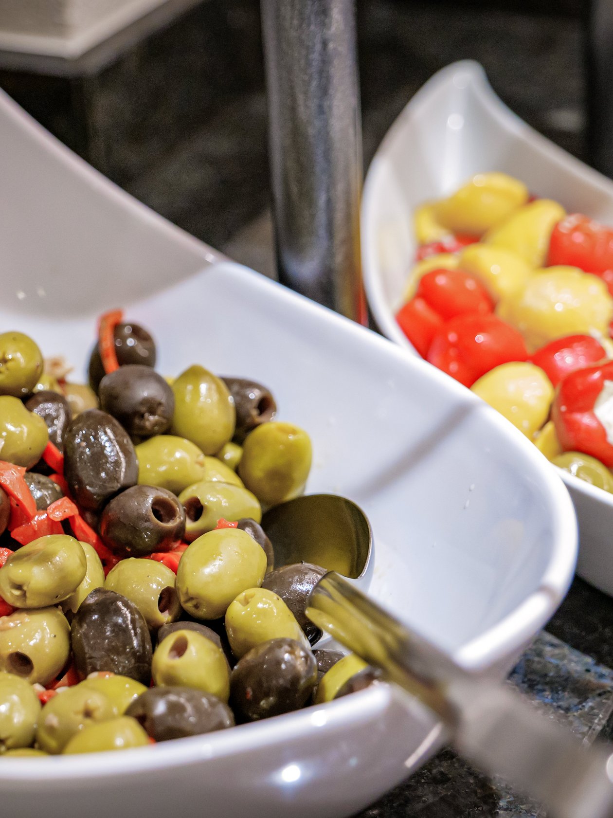 Gesunde Snacks im Buffet Zwei weiße Schalen mit einer Auswahl an Oliven und gefüllten Paprika auf einem Buffet