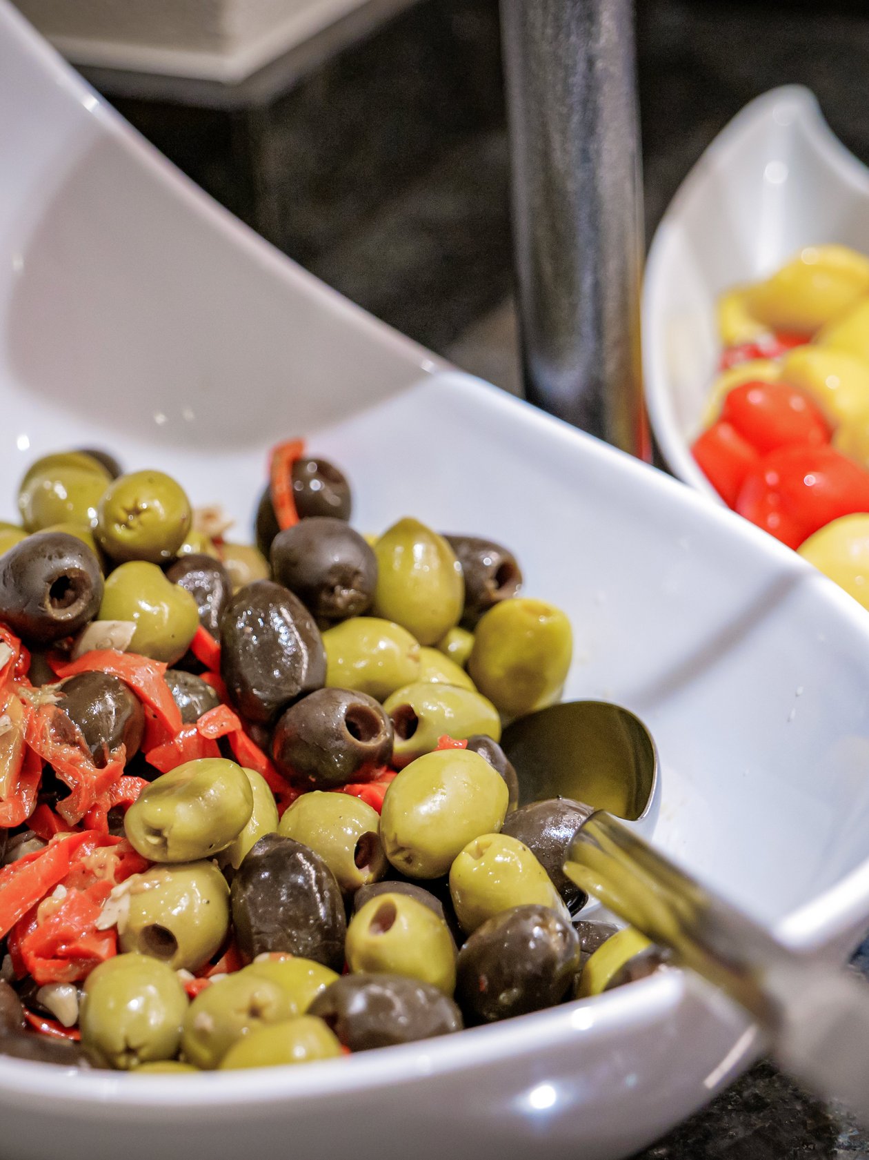 Gesunde Snacks im Buffet Zwei weiße Schalen mit einer Auswahl an Oliven und gefüllten Paprika auf einem Buffet