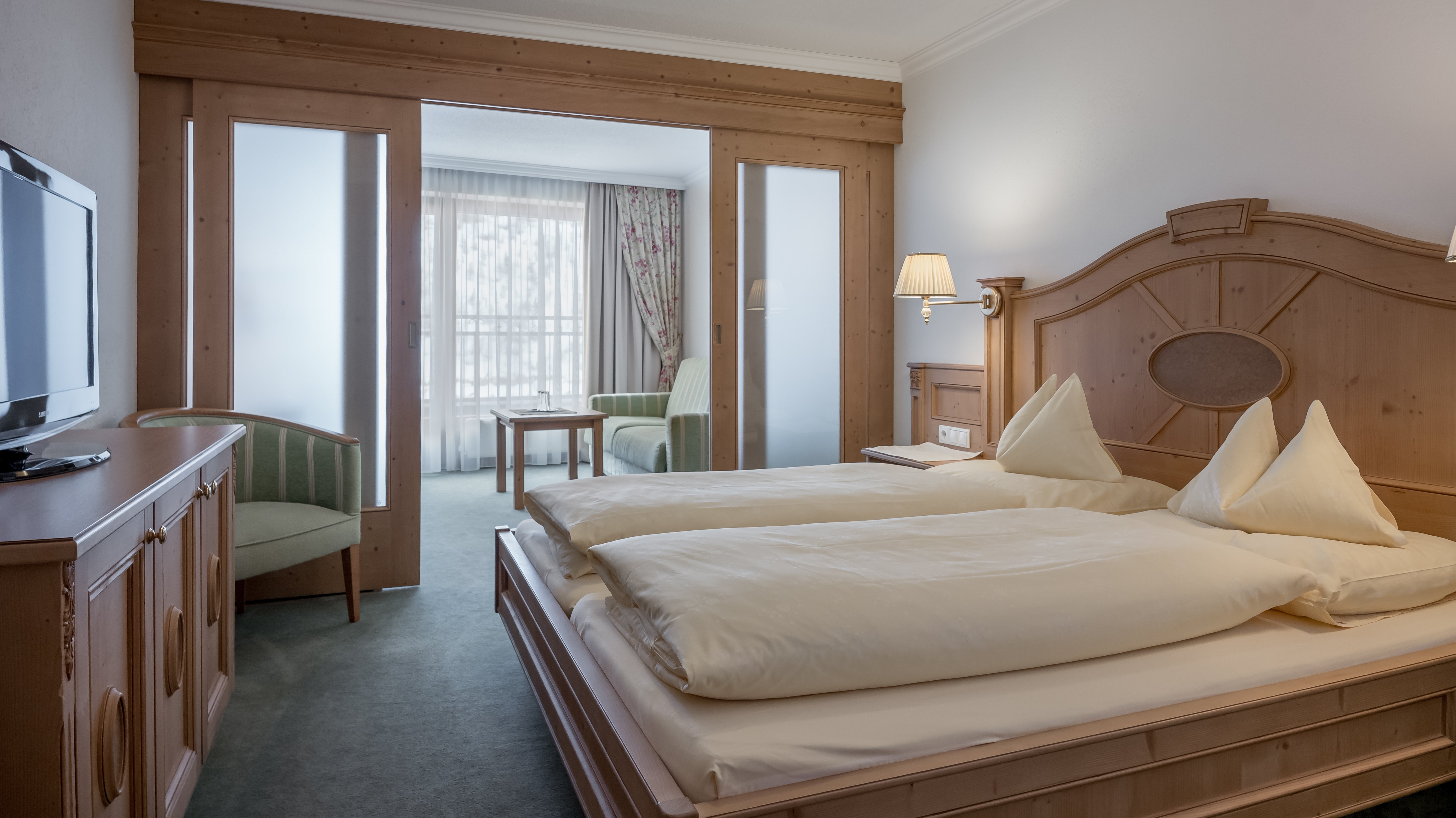Hotelzimmer mit Doppelbett, Fernseher und Sitzbereich unter großen Fenstern für Tageslicht.