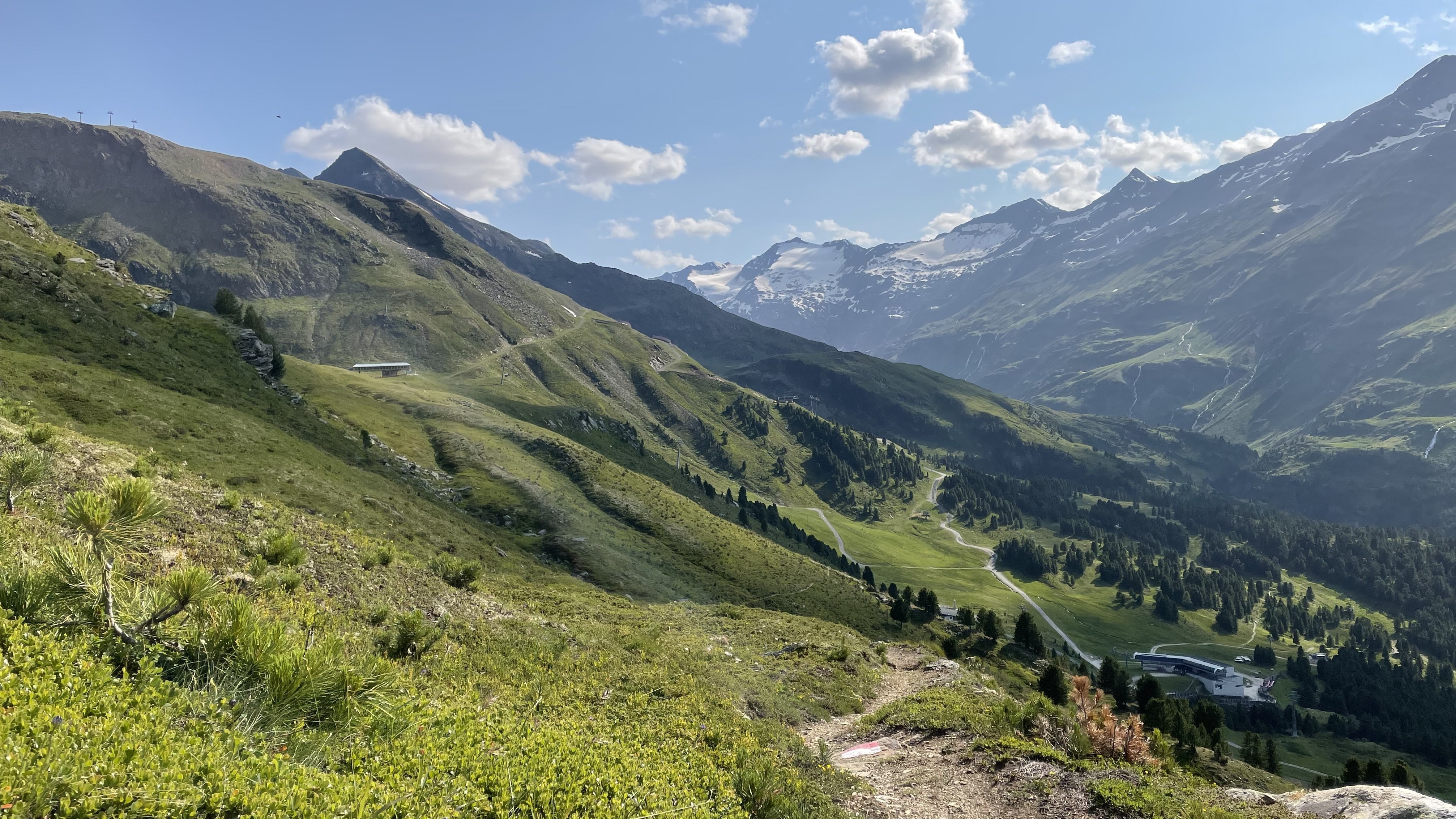 Panorama der Alpenlandschaft Berglandschaft mit schneebedeckten Gipfeln und grünen Hügeln unter blauem Himmel