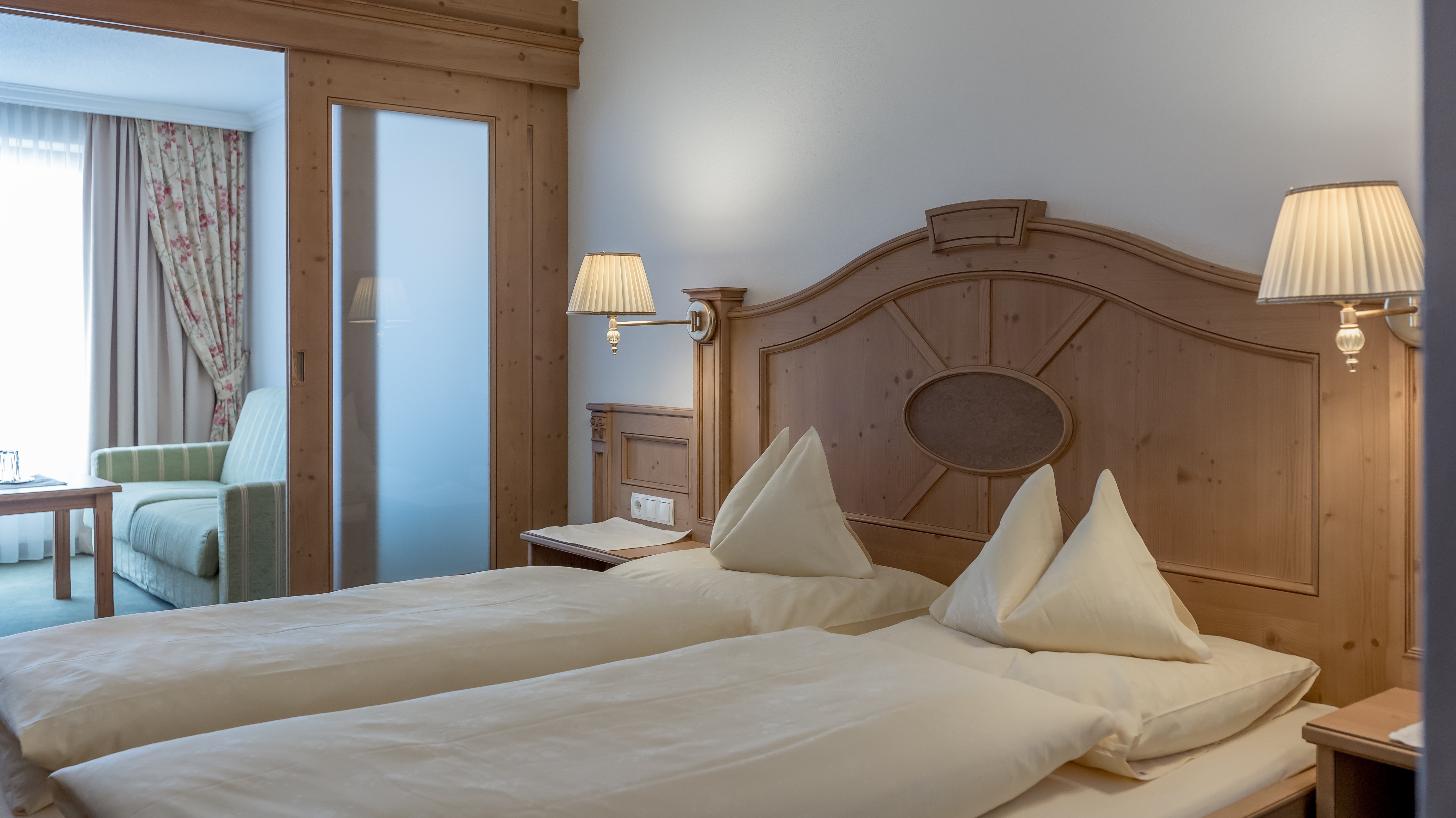 Moderne Unterkunft im Hotel Alpenland Hotelzimmer mit zwei Betten, dekorativen Kissen und Holzinterieur, Sitzecke im Hintergrund.