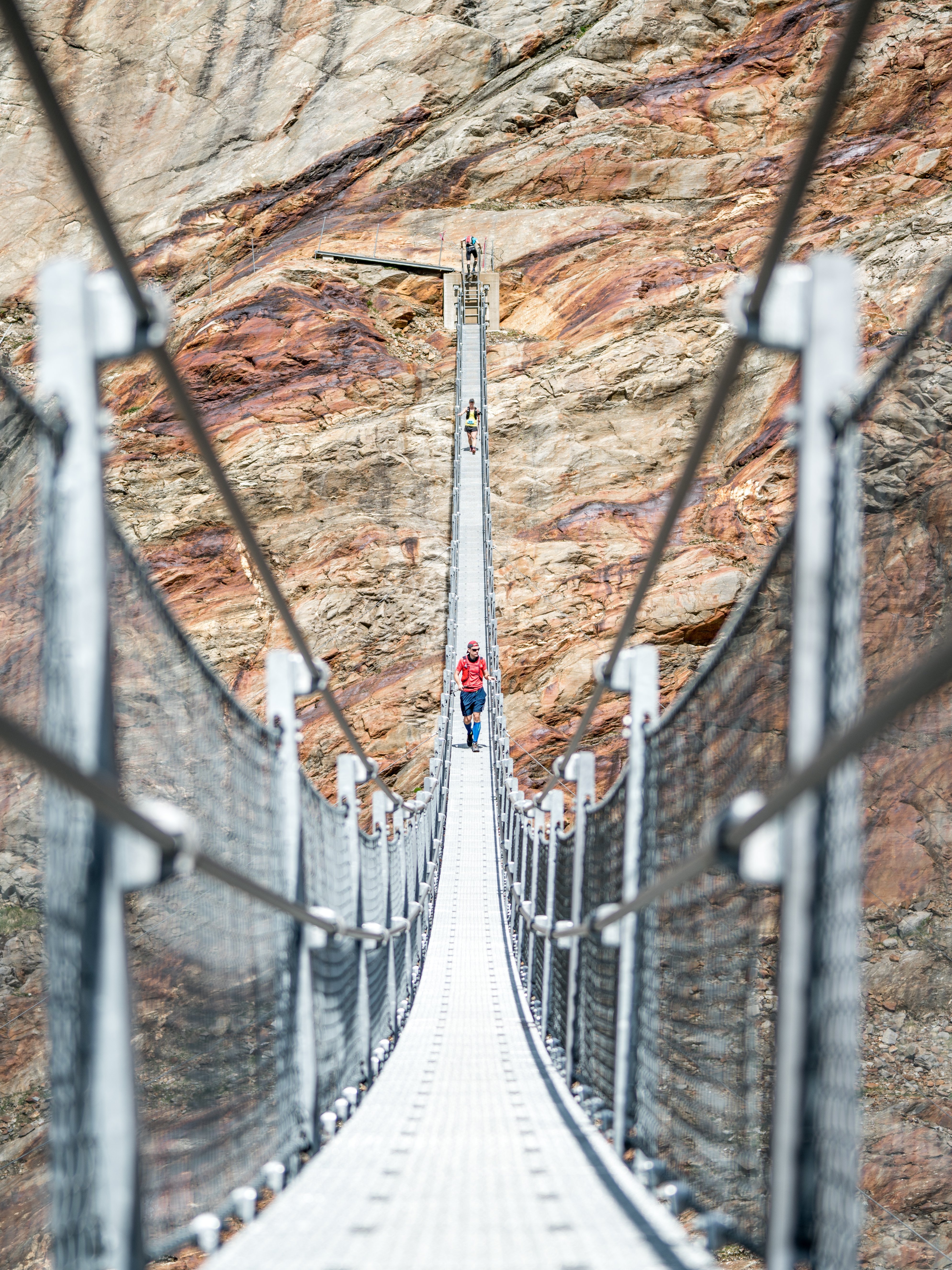 Eine Person läuft über eine Hängeseilbrücke, die sich über eine felsige Landschaft spannt.