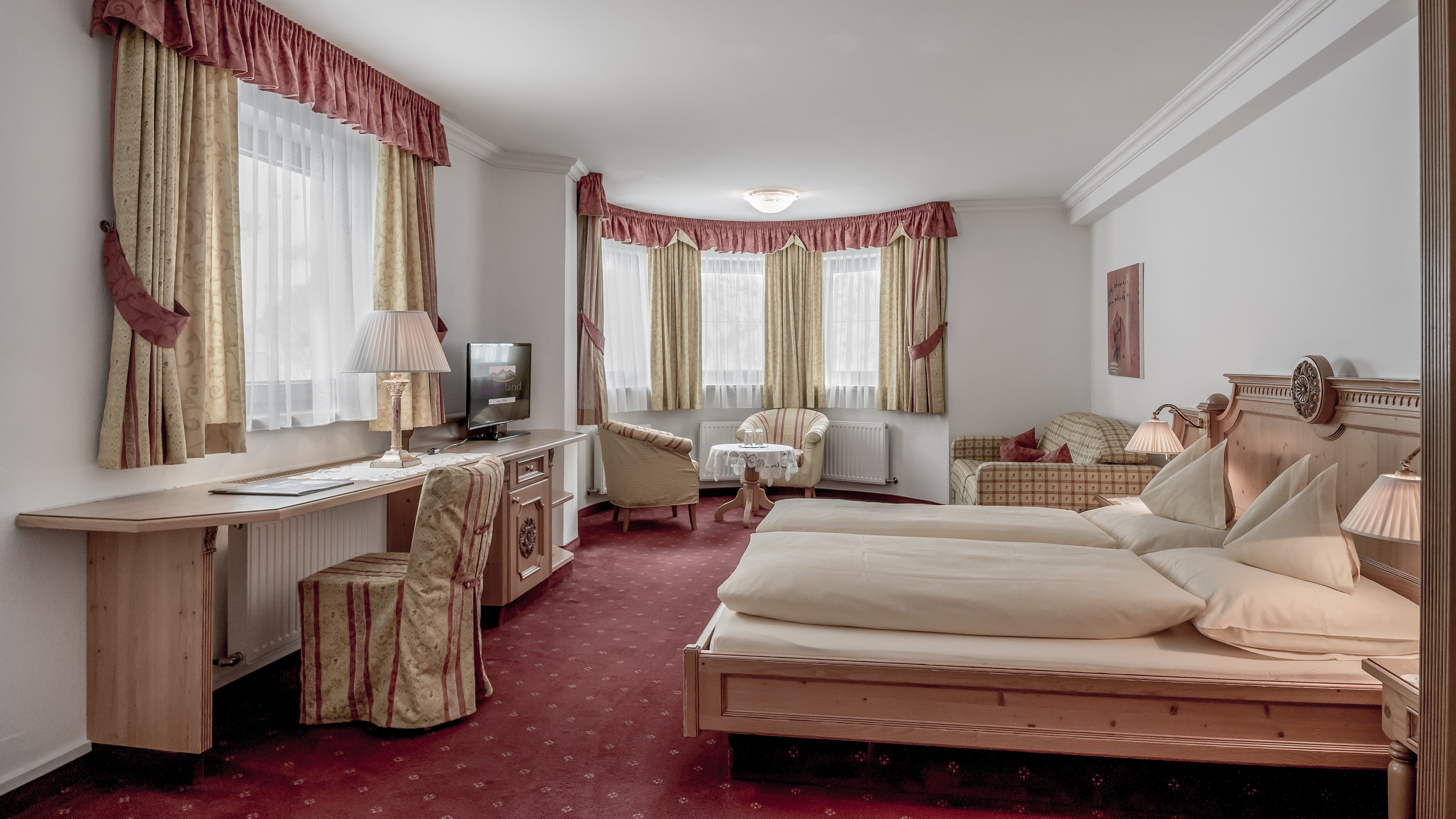 Luxuriöses Zimmer für unvergessliche Nächte Geräumiges Hotelzimmer mit Doppelbett, Sitzecke und großen Fenstern mit Vorhängen.