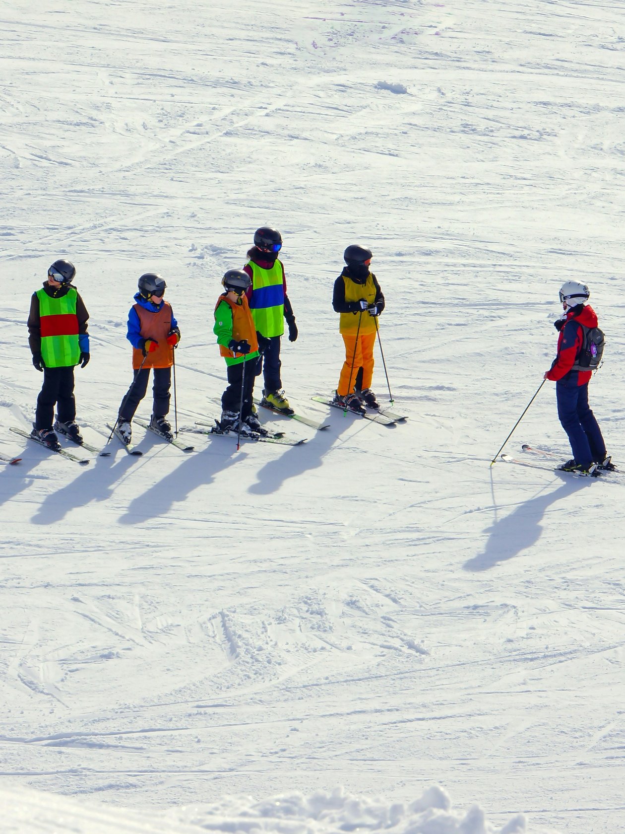 Gruppe von Skifahrern mit einem Lehrer auf einer verschneiten Piste in den Alpen