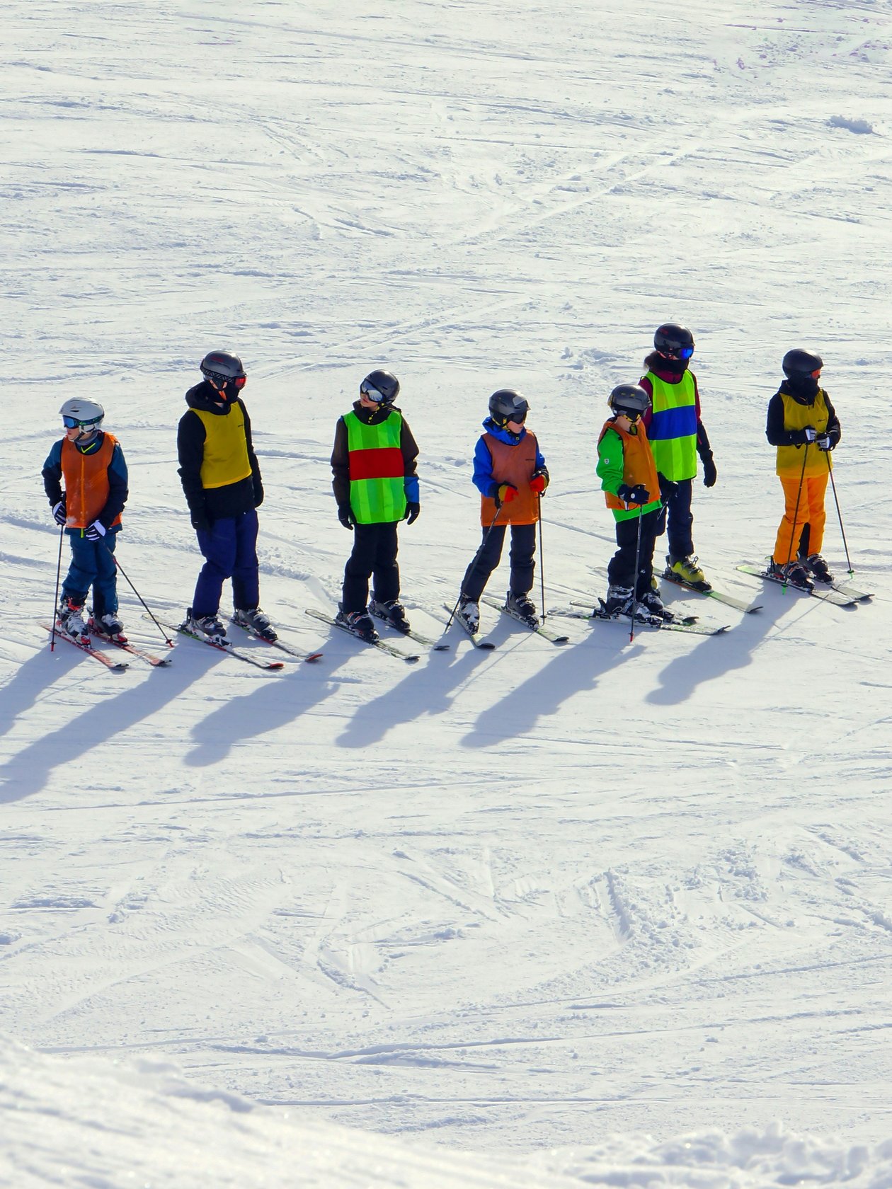 Gruppe von Skifahrern mit einem Lehrer auf einer verschneiten Piste in den Alpen