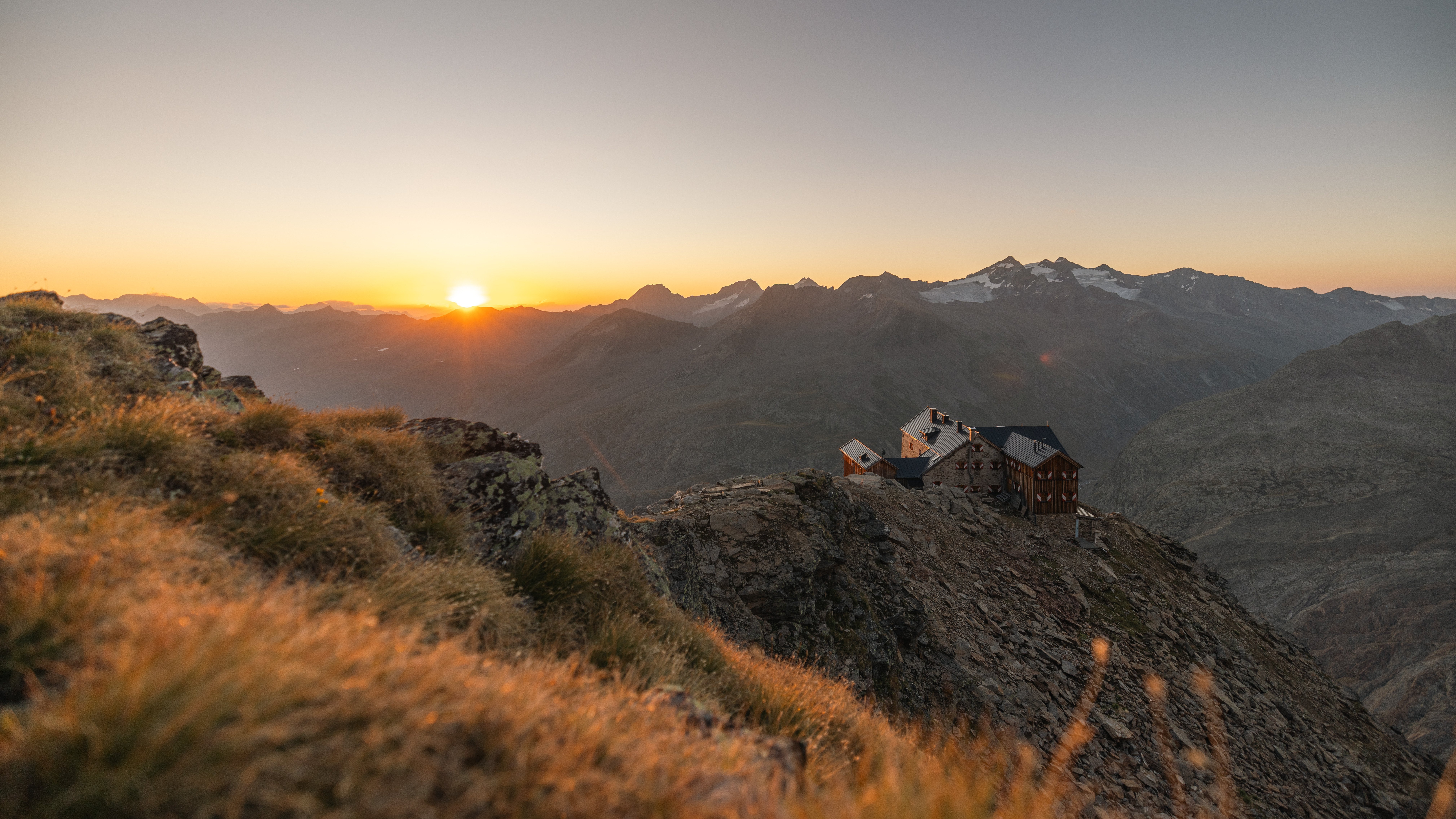 Alpine Idylle beim Sonnenaufgang Berglandschaft mit einer Berghütte auf einem Felsvorsprung und umliegenden Gipfeln
