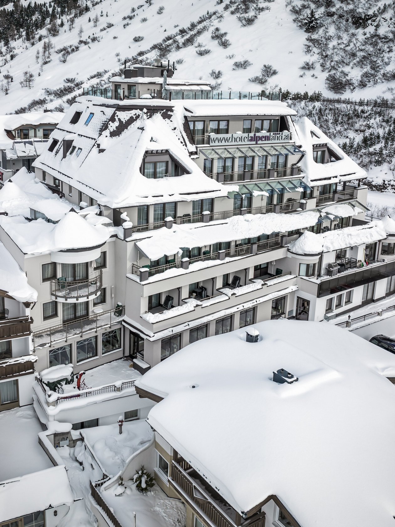 Verschneites Bergrefugium Luftaufnahme eines großen Hotels im Schnee, umgeben von Bergen, alpine Architektur.