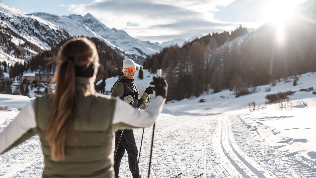 Langlauf im Schnee Zwei Personen fahren Langlauf auf einer verschneiten Strecke in den Bergen, umgeben von schneebedeckten Gipfeln.