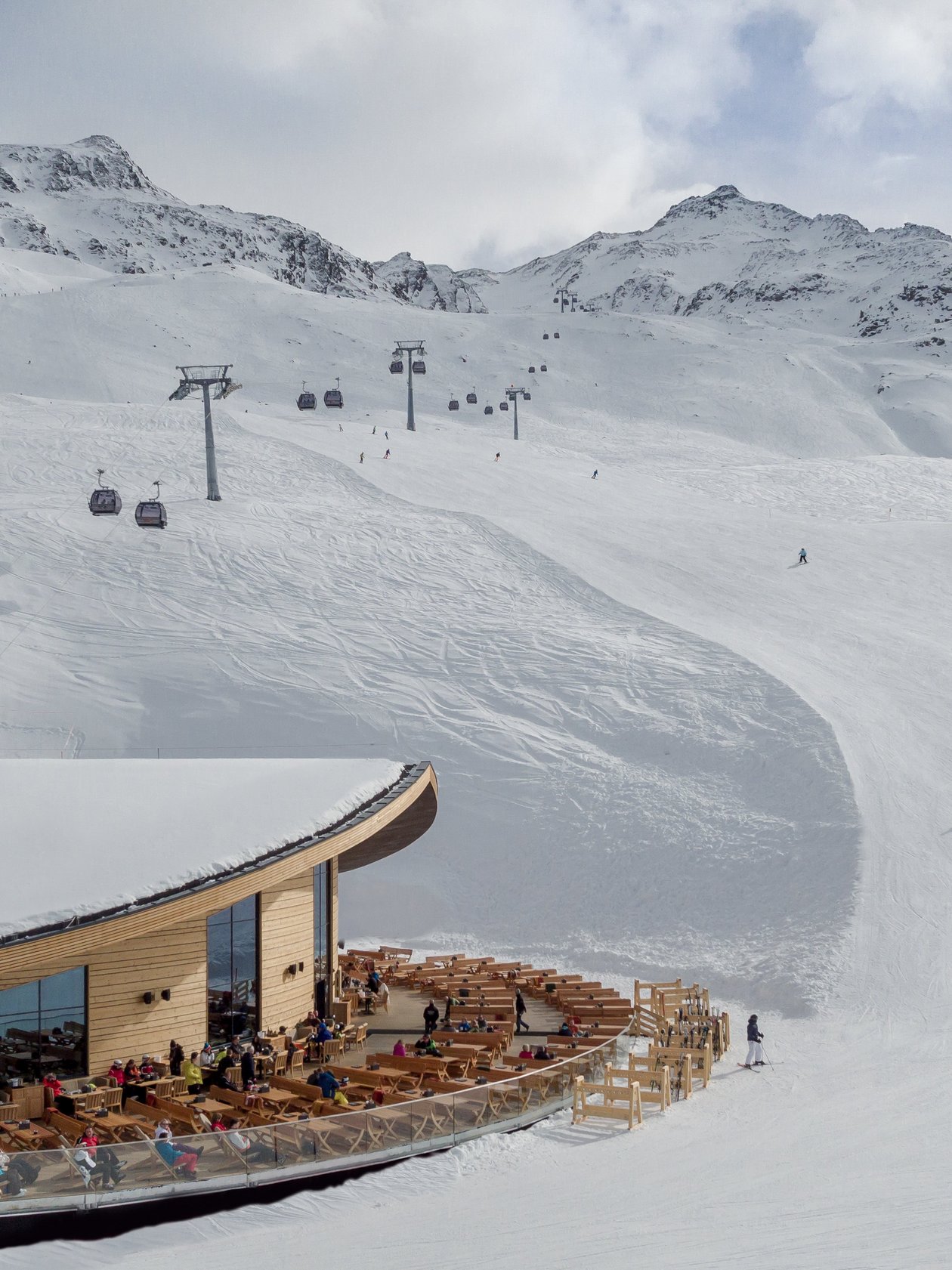 Schneeparadies für Skifahrer Moderne Gebäude mit Außenbereich in einem Skigebiet umgeben von verschneiten Bergen und Skiläufern.