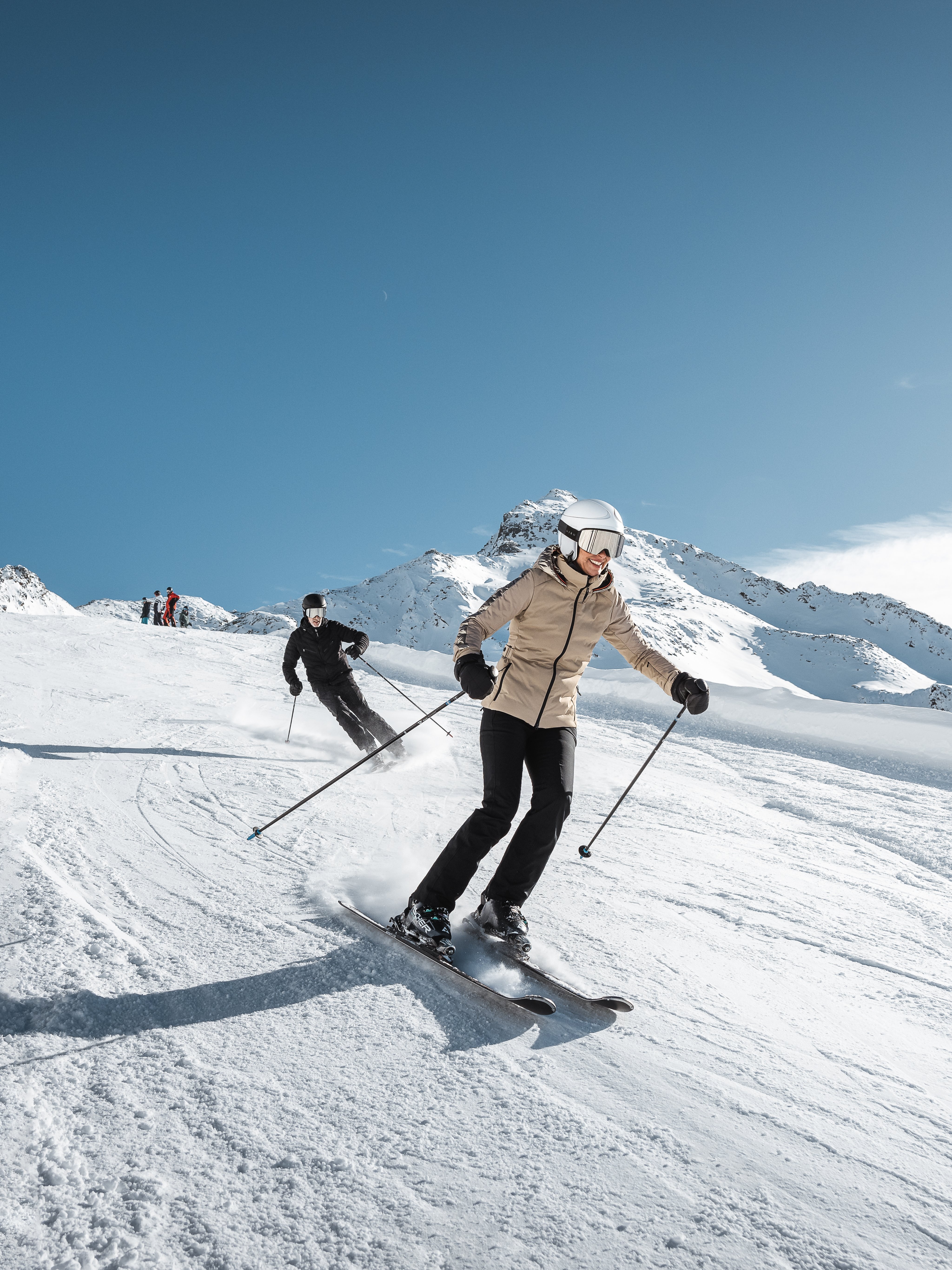 Skifahrer fahren eine schneebedeckte Abfahrt in den Bergen unter klarem Himmel hinunter