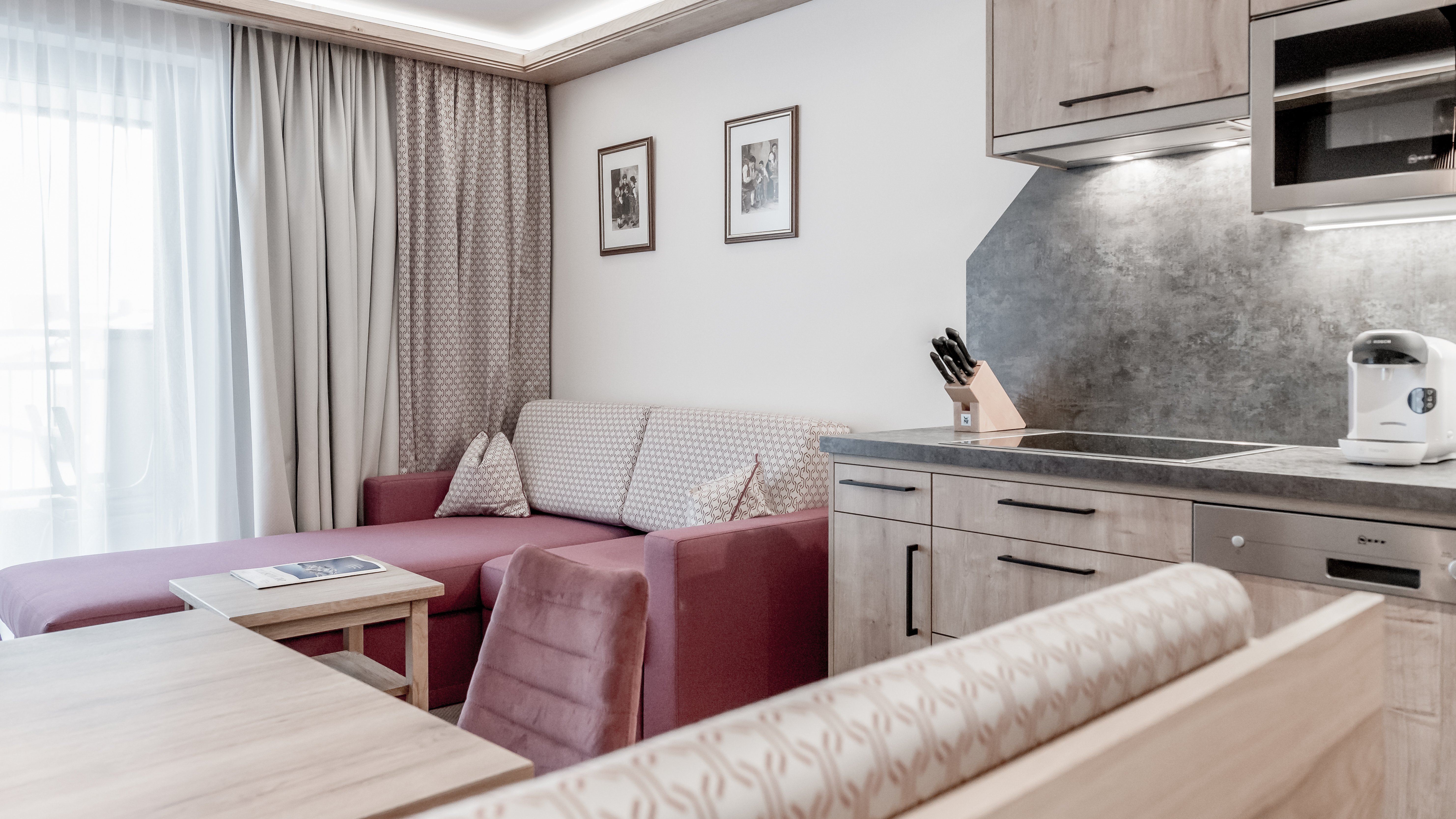 Moderne Apartmentgestaltung im Alpenland Wohnbereich mit Sofa, Esstisch und moderner Küche in einem Apartment mit Holzregalen und Geräten