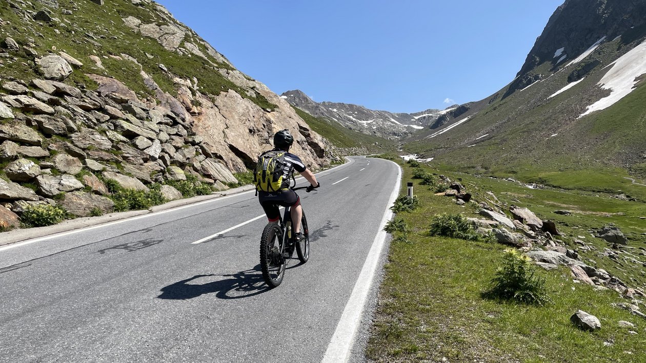 Person fährt Fahrrad auf kurvenreicher Straße in Berglandschaft mit Hügeln und Felsen.