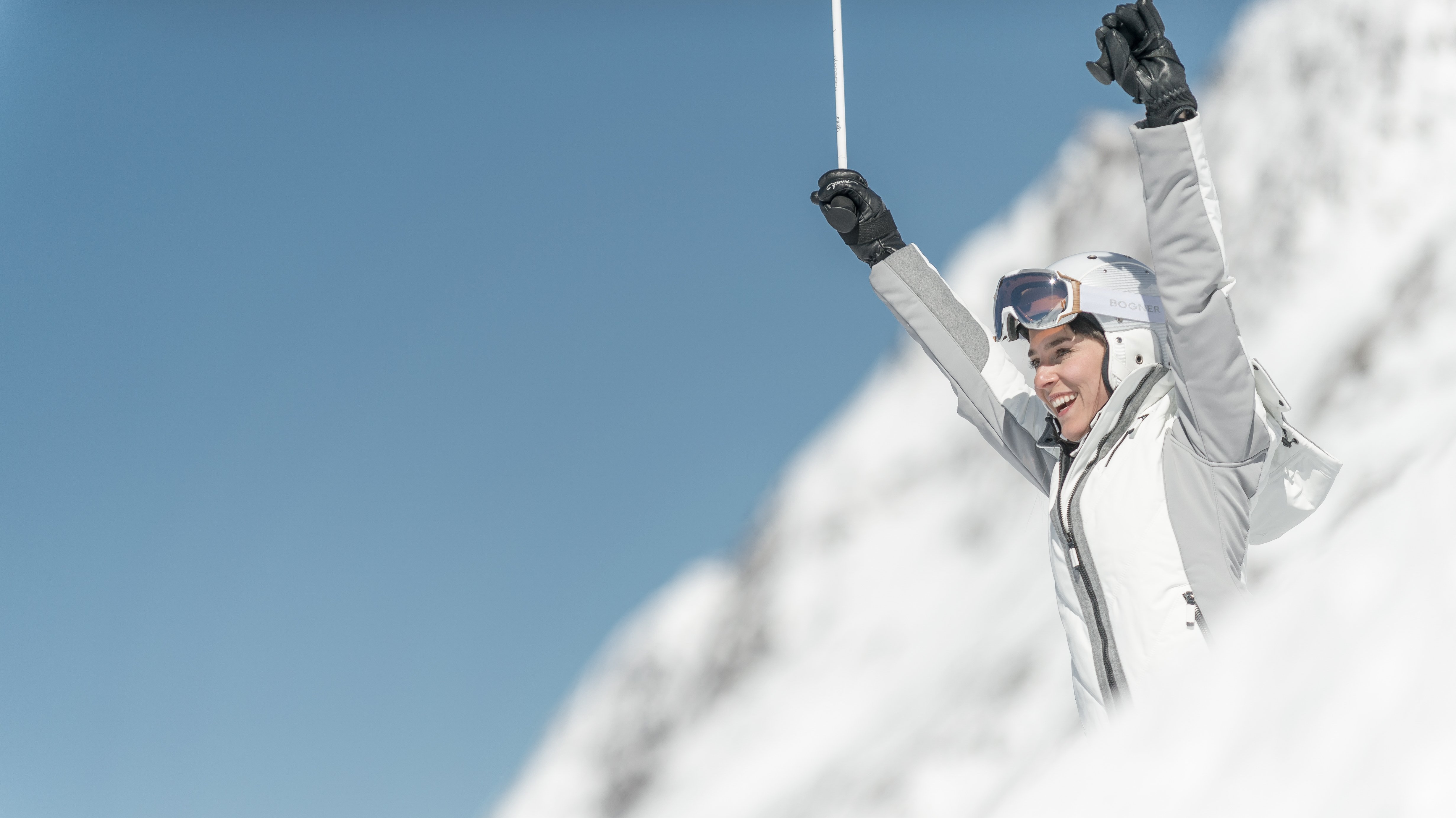 Person feiert auf einem schneebedeckten Berg mit Skiausrüstung und Skistöcken in der Hand.
