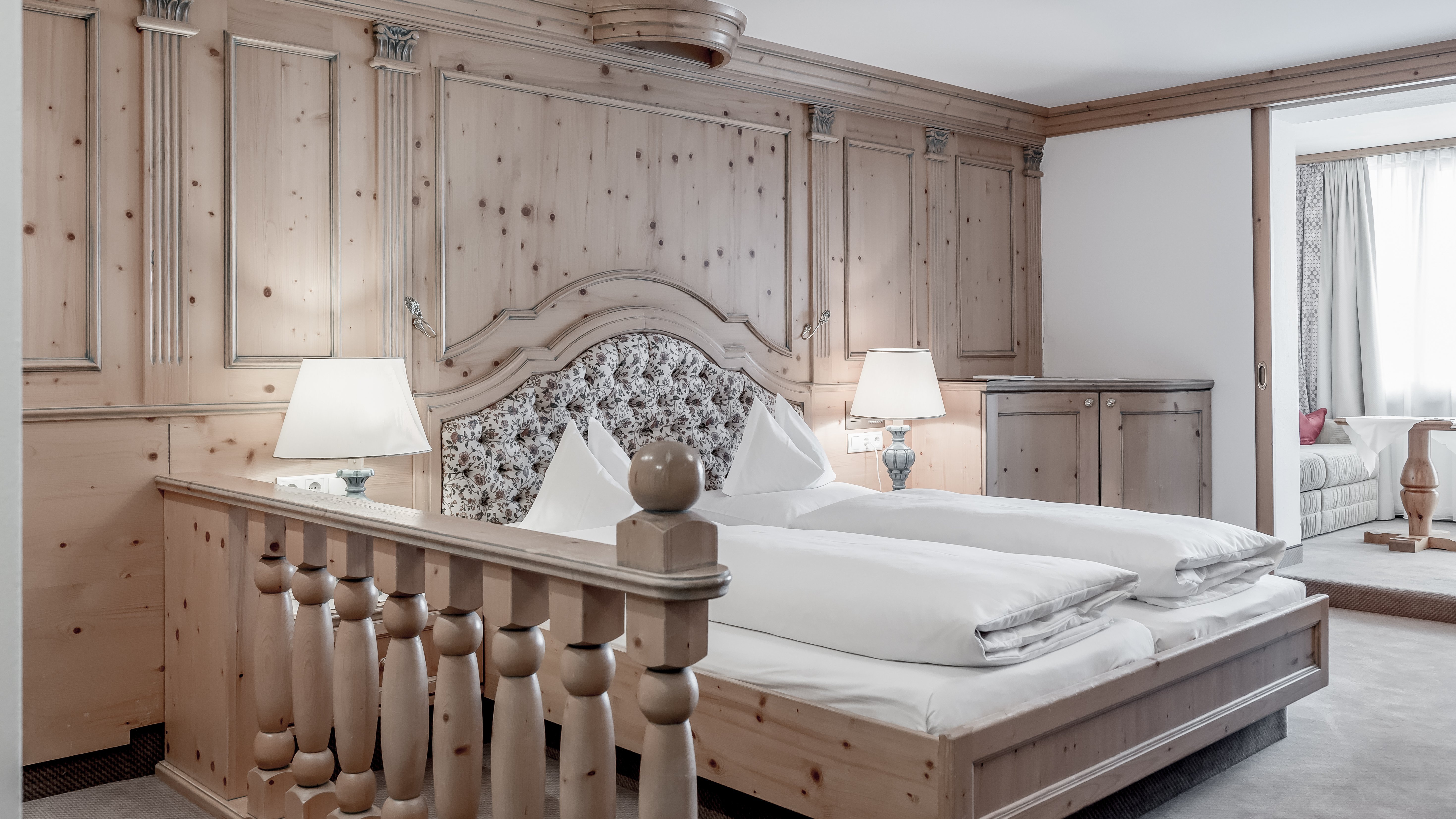 Luxuriöse Unterbringung im Alpenland Hotelzimmer mit Holzverkleidung, Doppelbett und Nachttischlampen in einem eleganten Design.