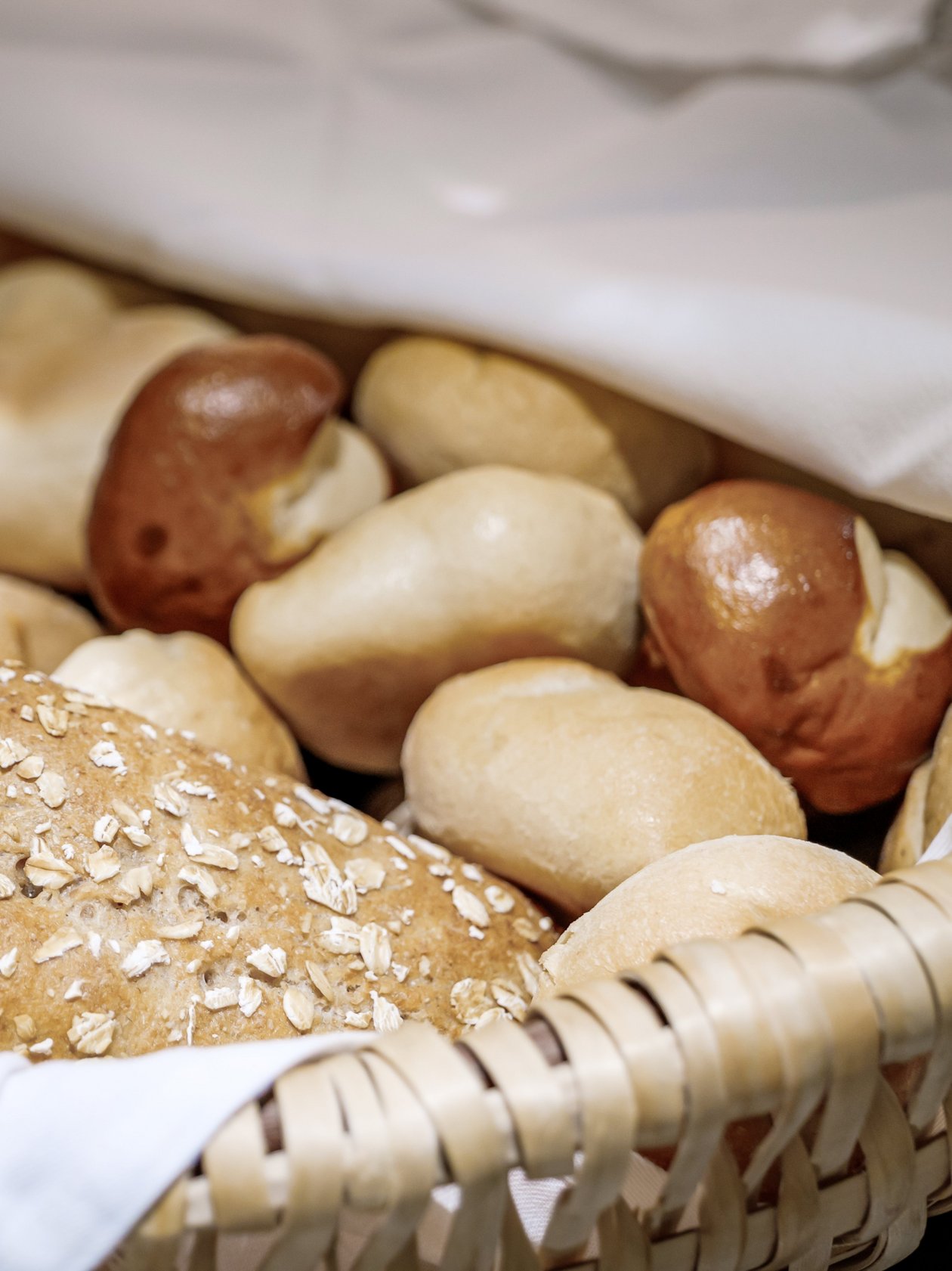 Frische Brötchen im Korb Ein geflochtener Korb mit verschiedenen Brötchen, darunter Brezeln und Haferbrot.