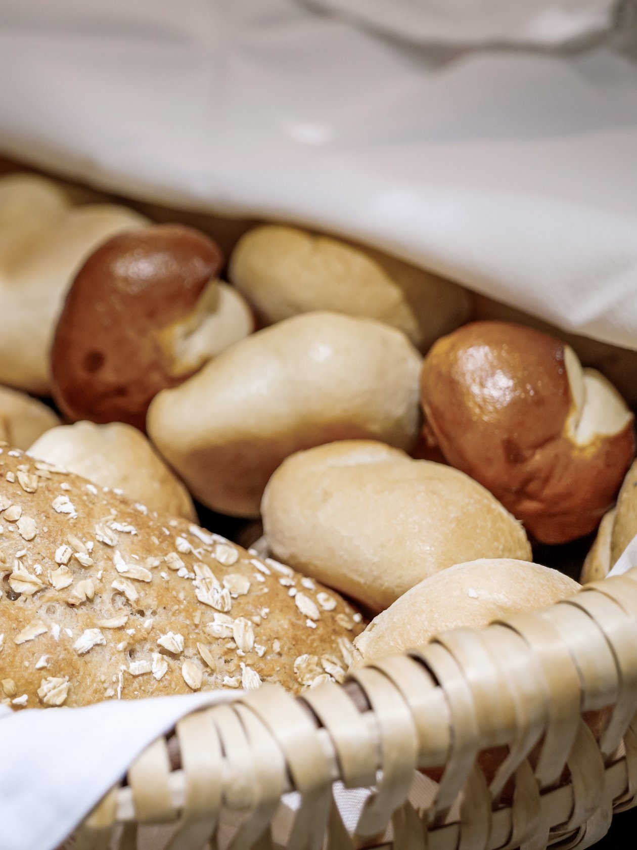 Frische Brötchen im Korb Ein geflochtener Korb mit verschiedenen Brötchen, darunter Brezeln und Haferbrot.