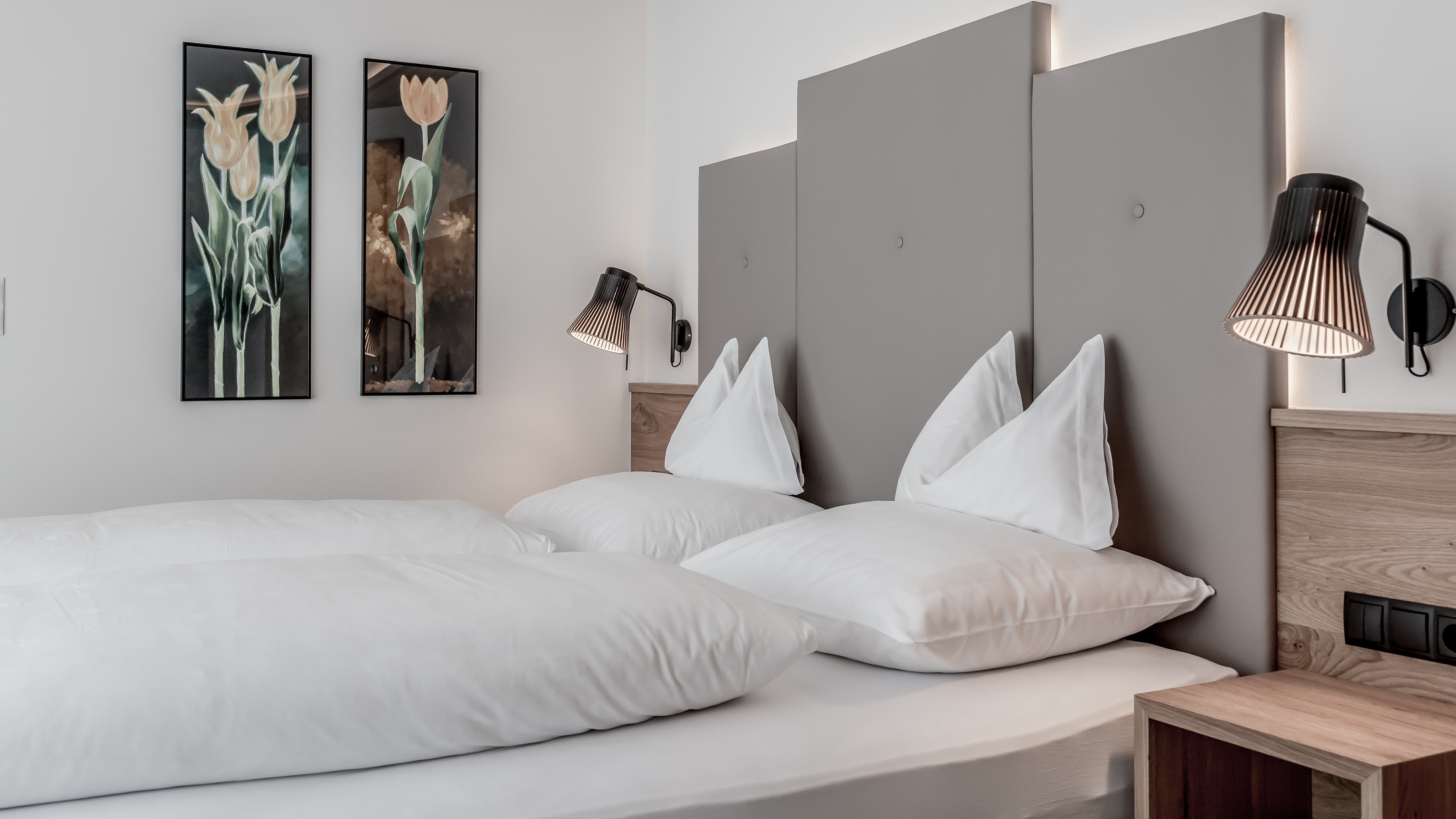 Moderne Eleganz im Hotelzimmer Hotelzimmer mit Doppelbett, weißen Bettbezügen und dekorativen Wandlampen, floralem Kunstwerk.
