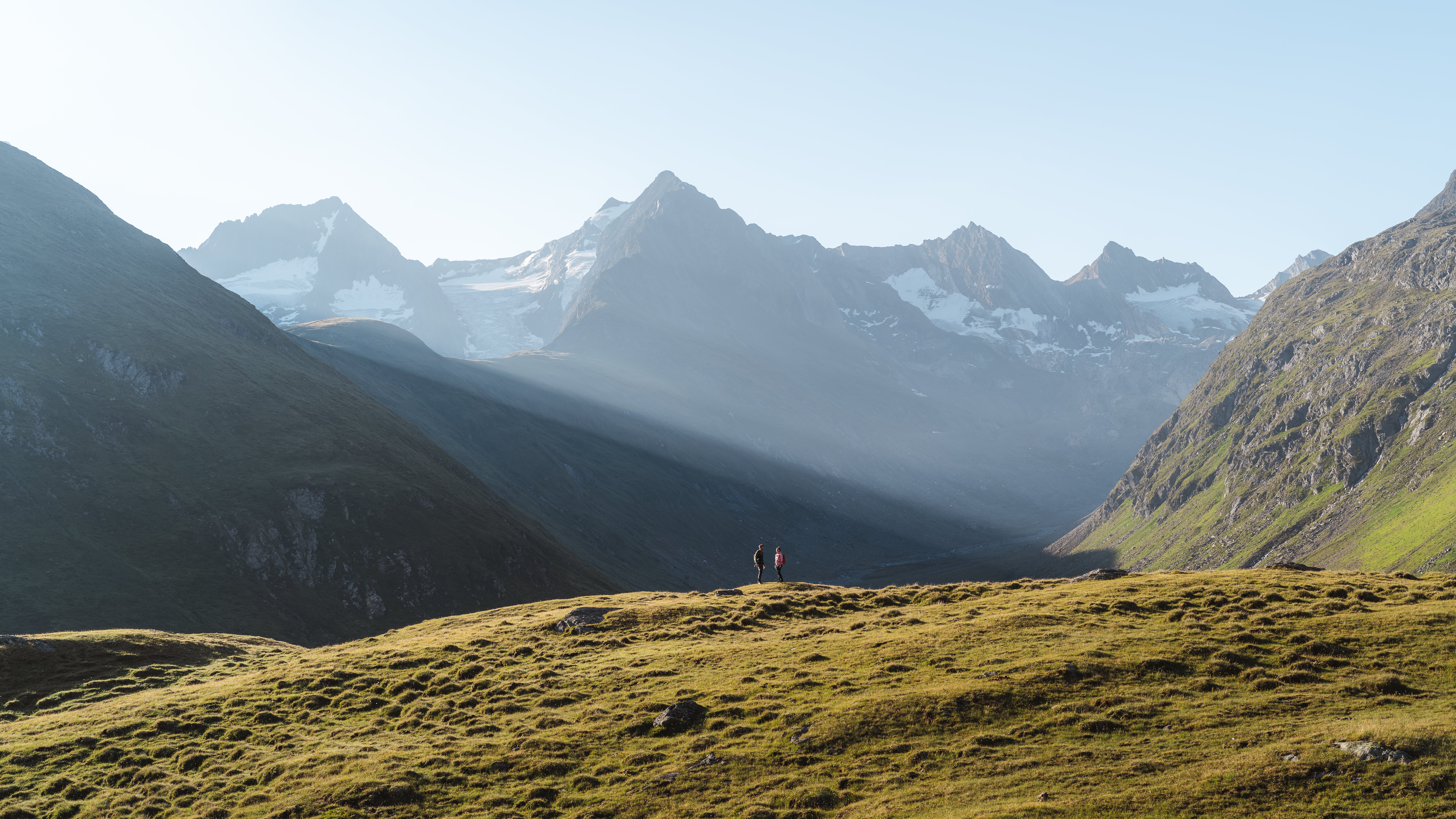 Hiking in der Berglandschaft Zwei Wanderer erkunden eine weite Berglandschaft mit schneebedeckten Gipfeln und klarem Himmel.