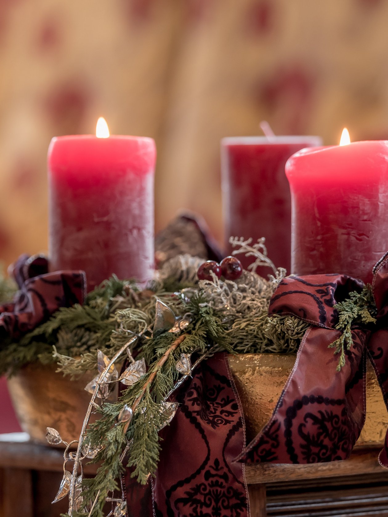 Four red candles in a golden bowl surrounded by greenery and purple ribbons for holiday decoration