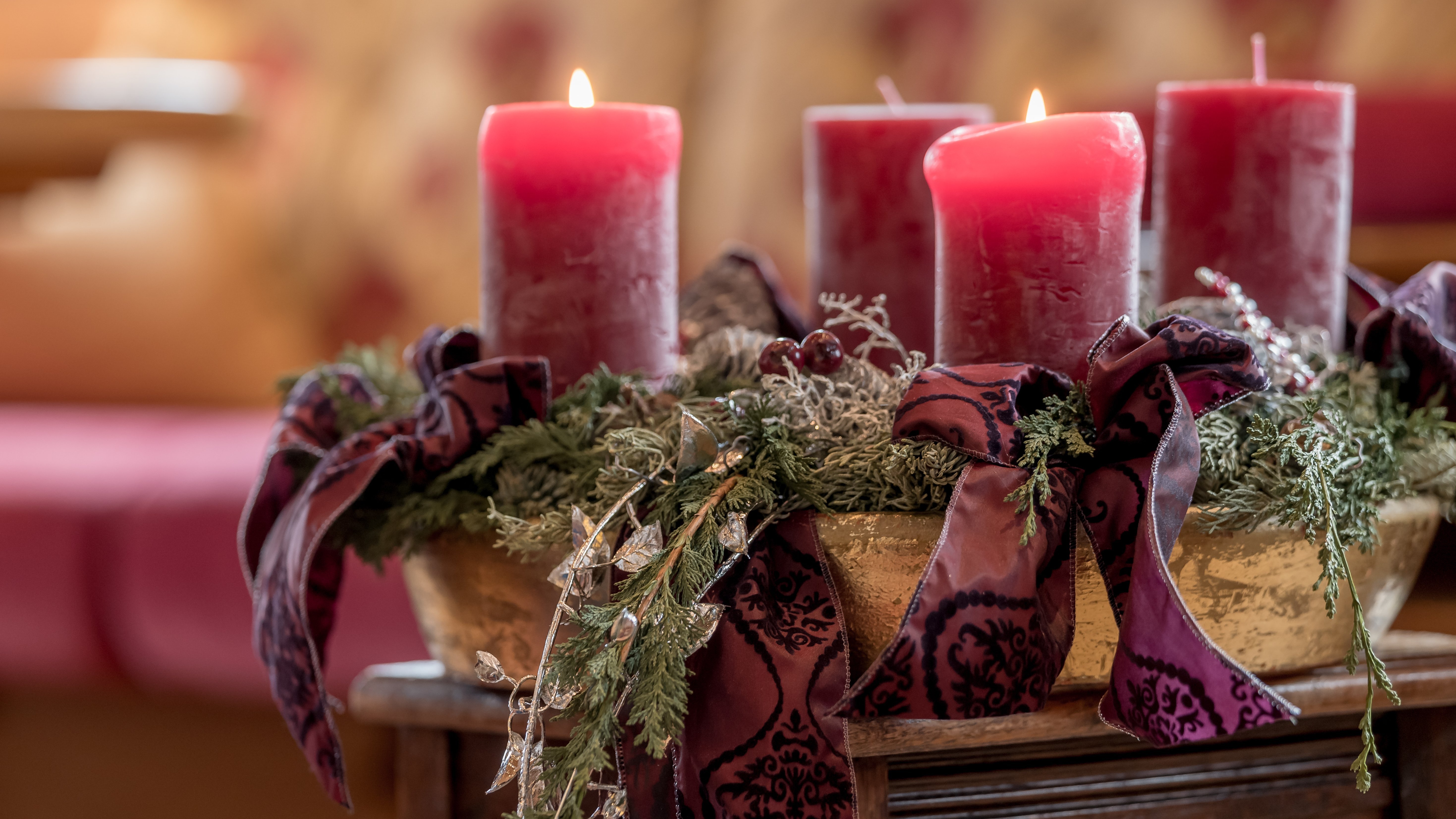Festliche Kerzenarrangement Vier rote Kerzen auf einem Adventskranz mit grünem Laub und Bändern in einem gemütlichen Raum.