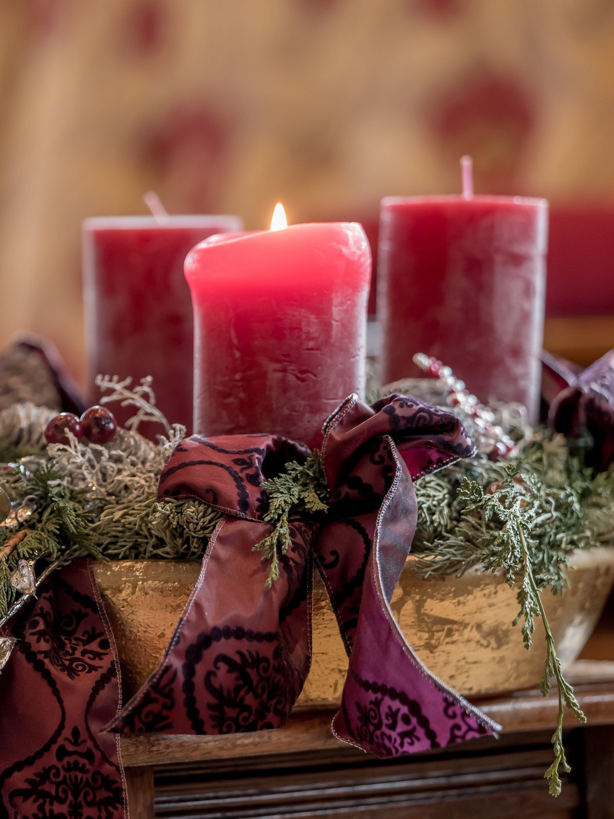 Festliche Kerzenarrangement Vier rote Kerzen auf einem Adventskranz mit grünem Laub und Bändern in einem gemütlichen Raum.