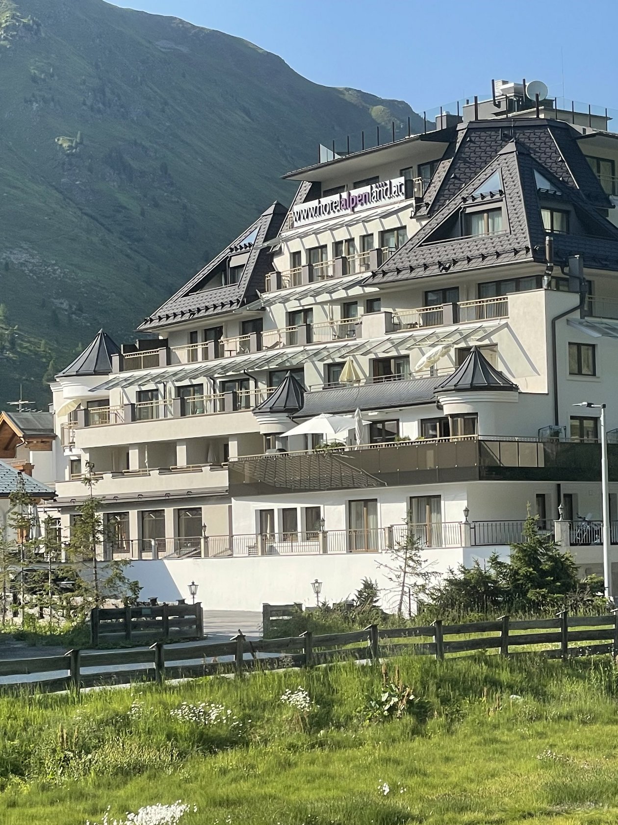 Mehrstöckiges Hotelgebäude in gebirgiger Umgebung mit umliegendem Grün und klarem Himmel