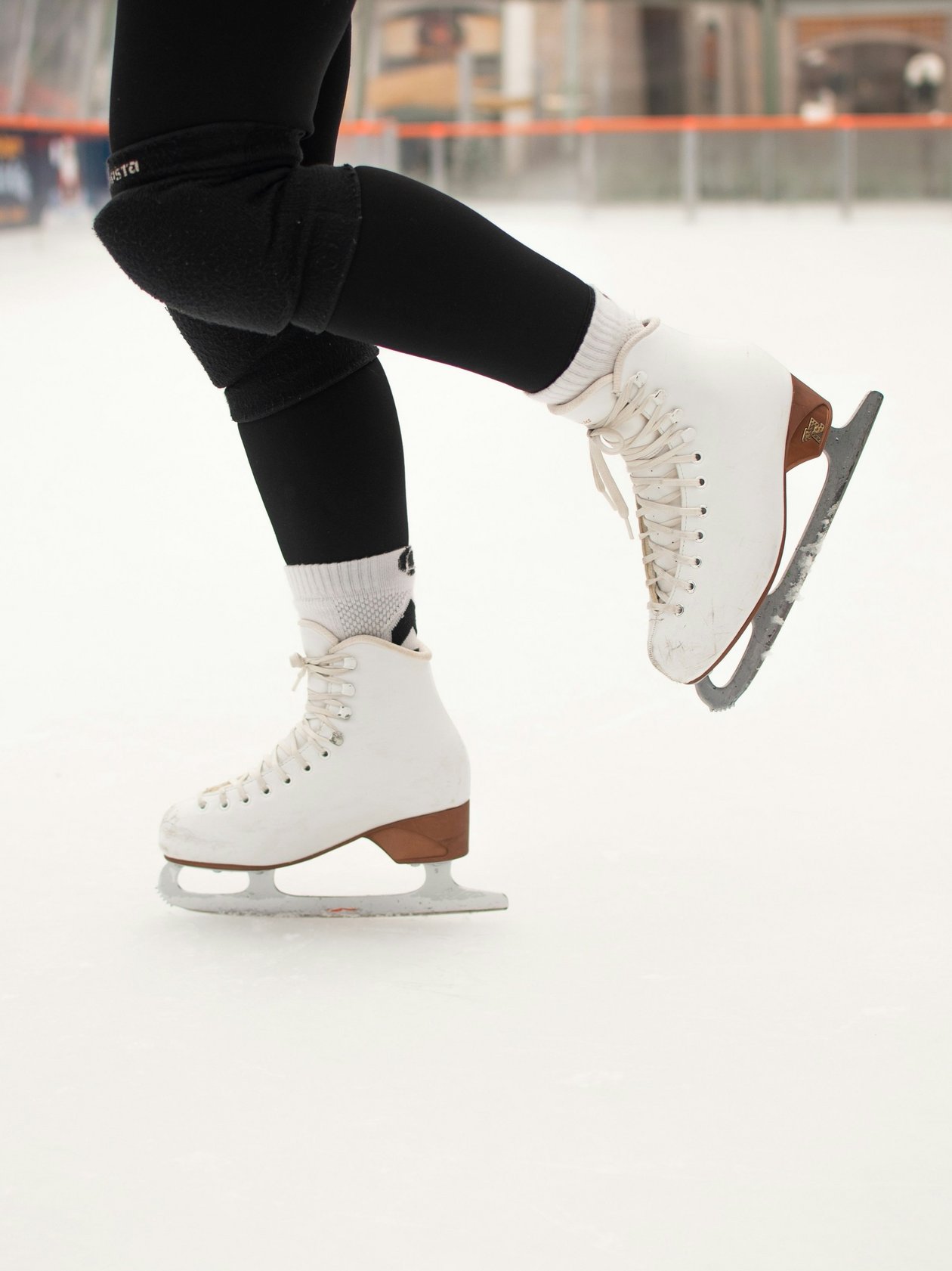 Nahaufnahme einer Person mit weißen Eiskunstlauf-Schlittschuhen auf einer Eisfläche.