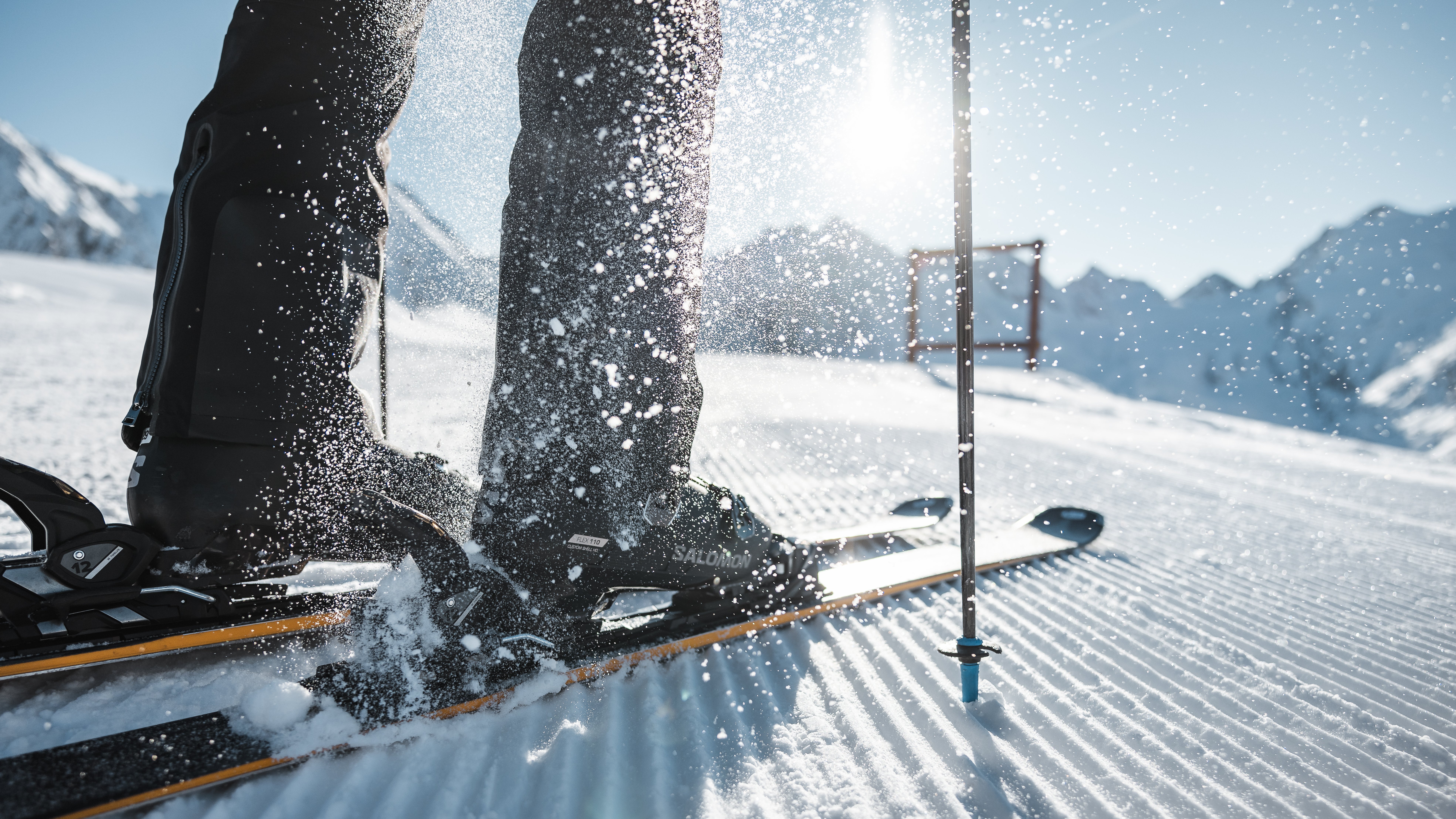 Nahaufnahme von Skifahrerfüßen auf Skiern mit Schnee um sie herum vor Berglandschaft.
