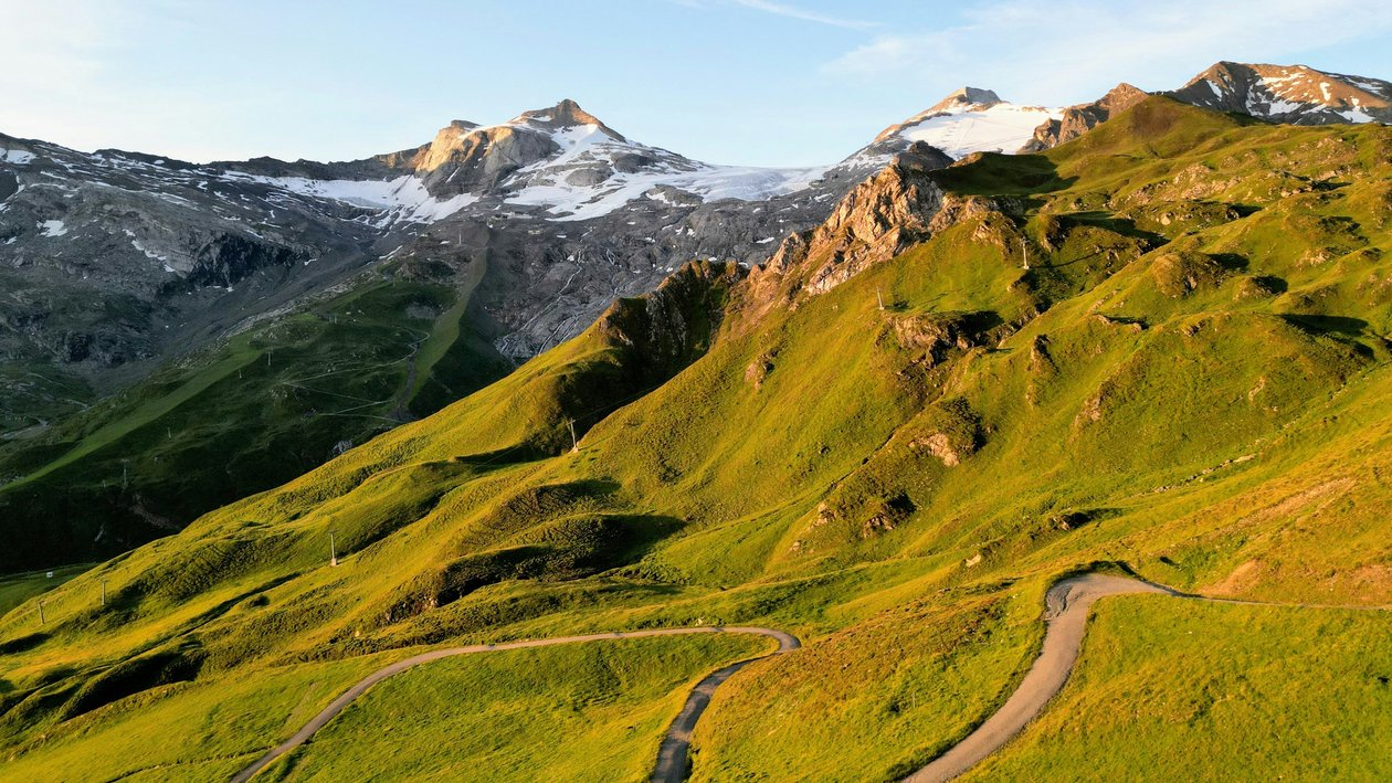 Blick auf schneebedeckte Berge mit grünen Hügeln im Vordergrund unter klarem Himmel
