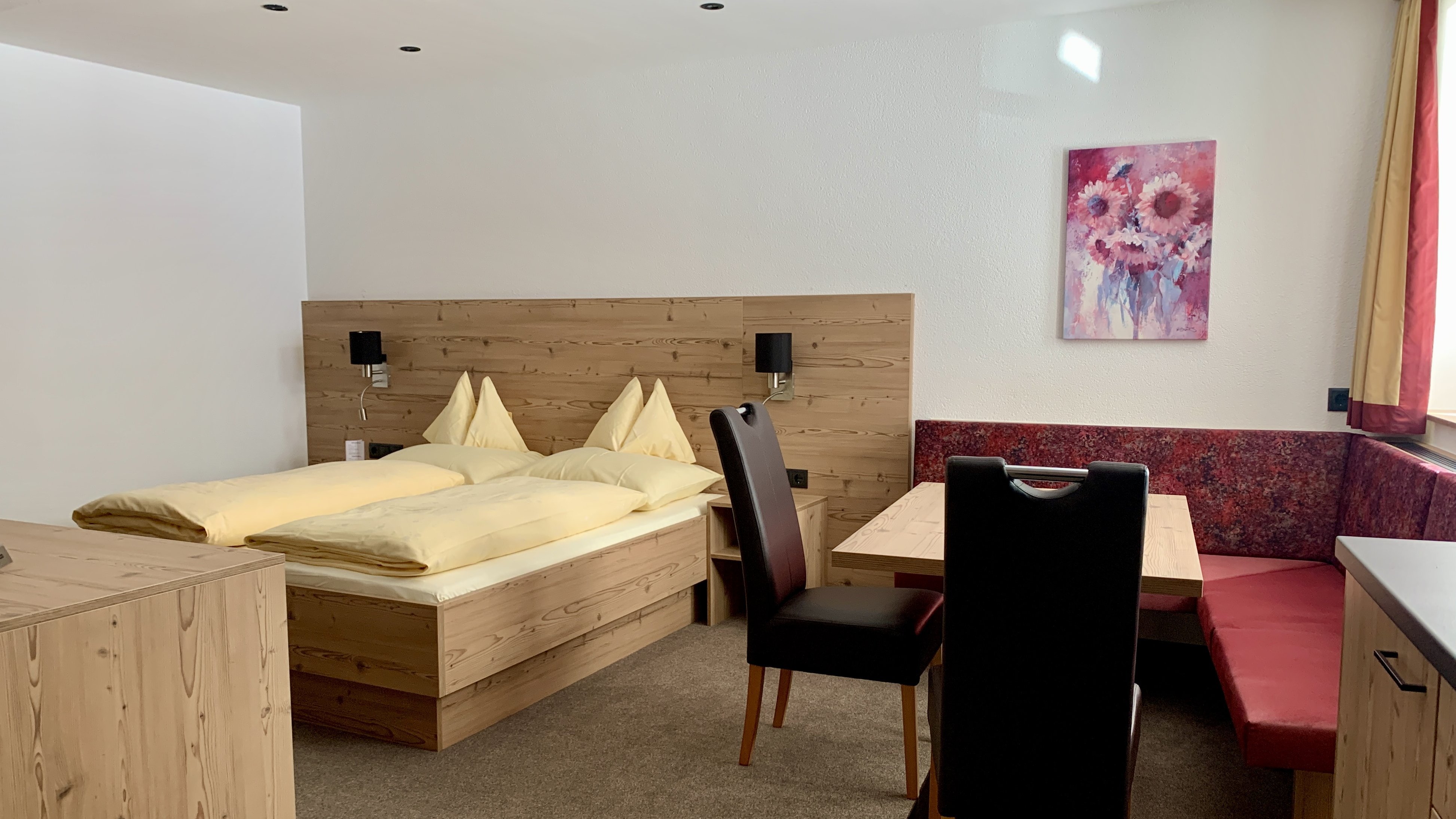 Gemütliches Zimmer im Hotel Alpenland Hotelzimmer mit Doppelbett, Essbereich und Holzinterieur in alpinem Design ohne sichtbare Marken.