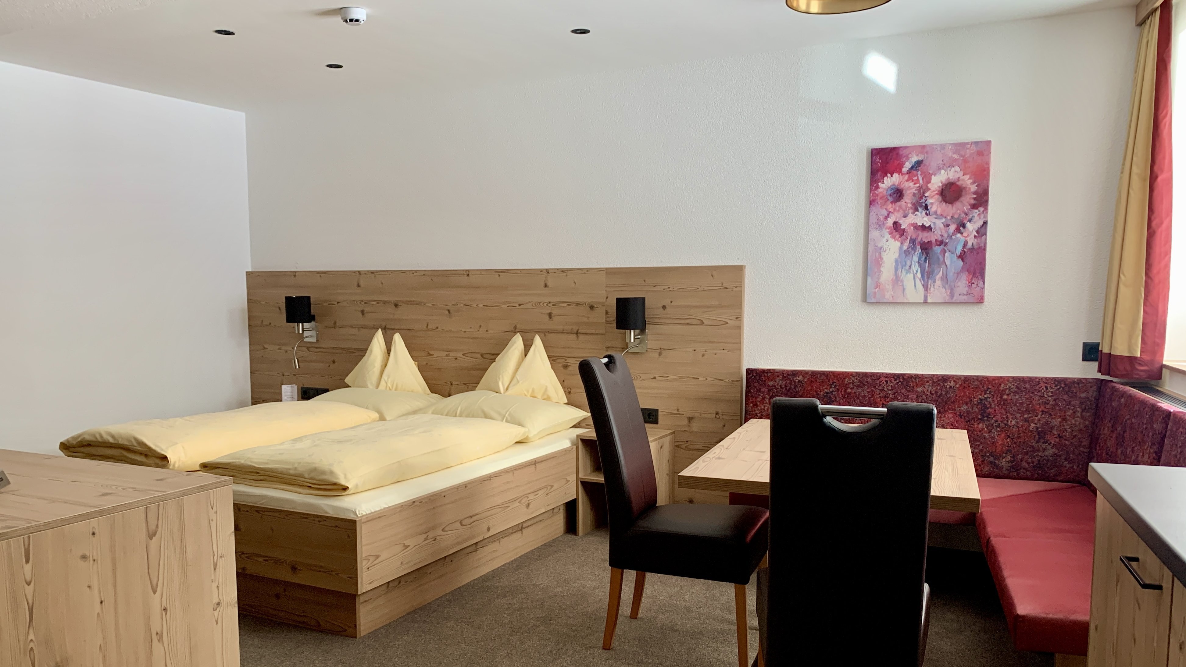 Hotelzimmer mit Doppelbett, Essbereich und Holzinterieur in alpinem Design ohne sichtbare Marken.