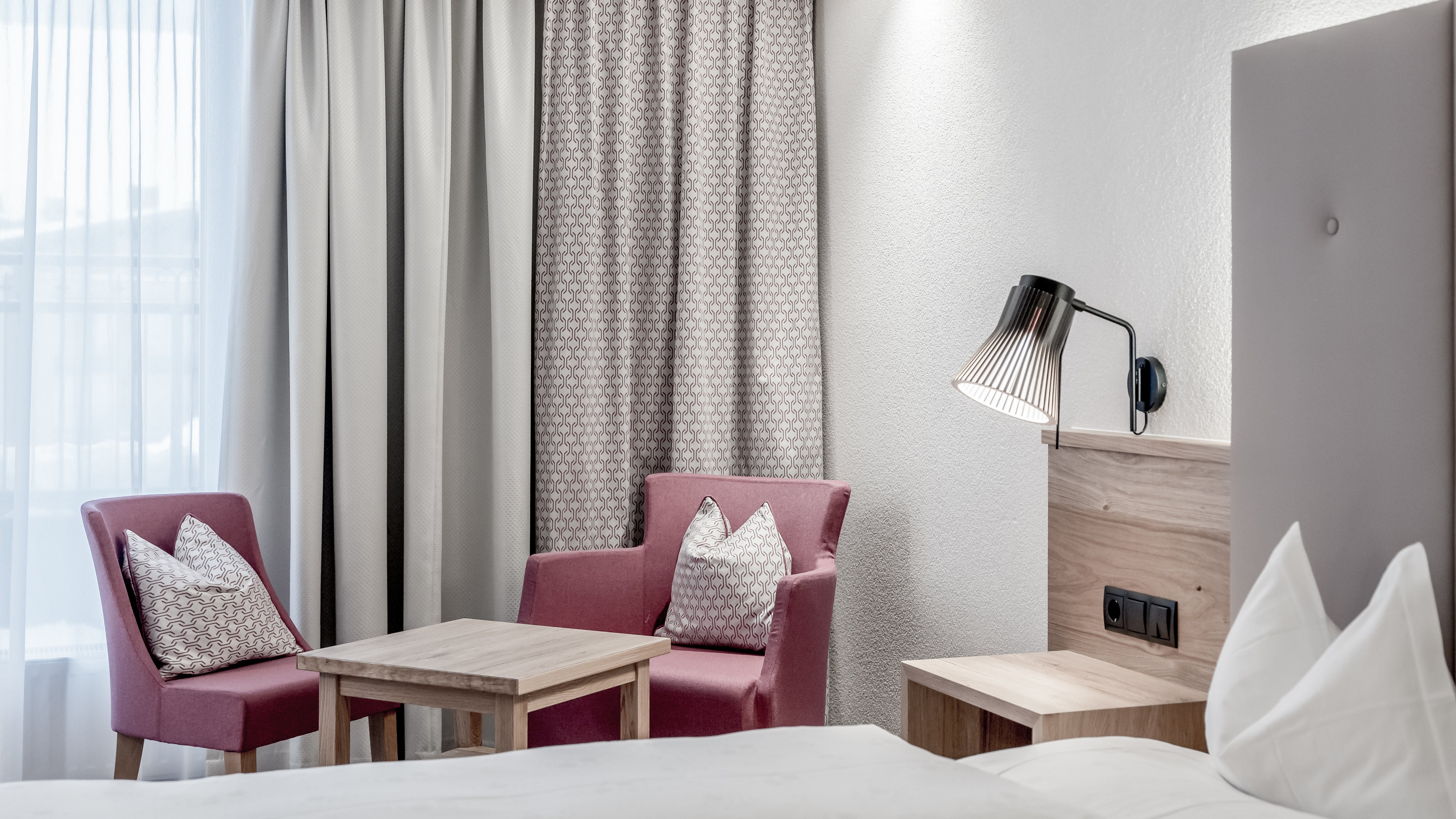 Modernes Zimmer für Wohlfühlmomente Helles Hotelzimmer mit zwei pinken Stühlen und einem Holzstisch vor einem Fenster.