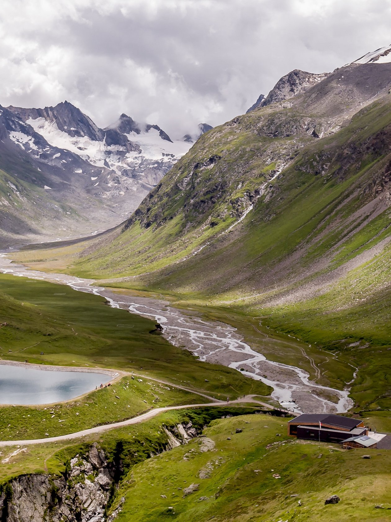 Atemberaubende Berglandschaft mit glacialem See Große Berglandschaft mit einem glacialen See und saftig grünen Tälern unter wolkigem Himmel.