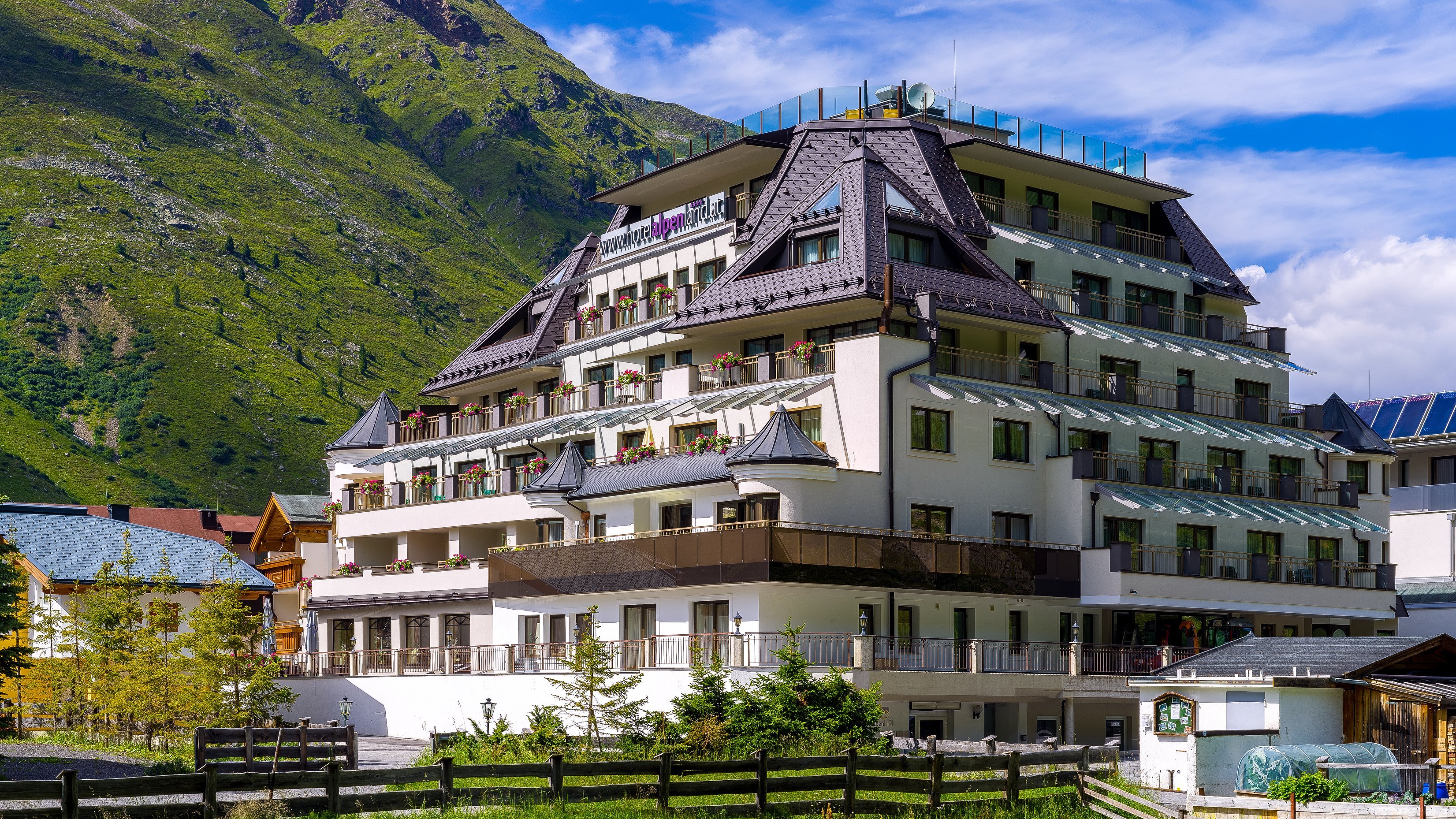 Mehrstöckiges Gebäude umgeben von Bergen und Bäumen unter klarem Himmel in Obergurgl.