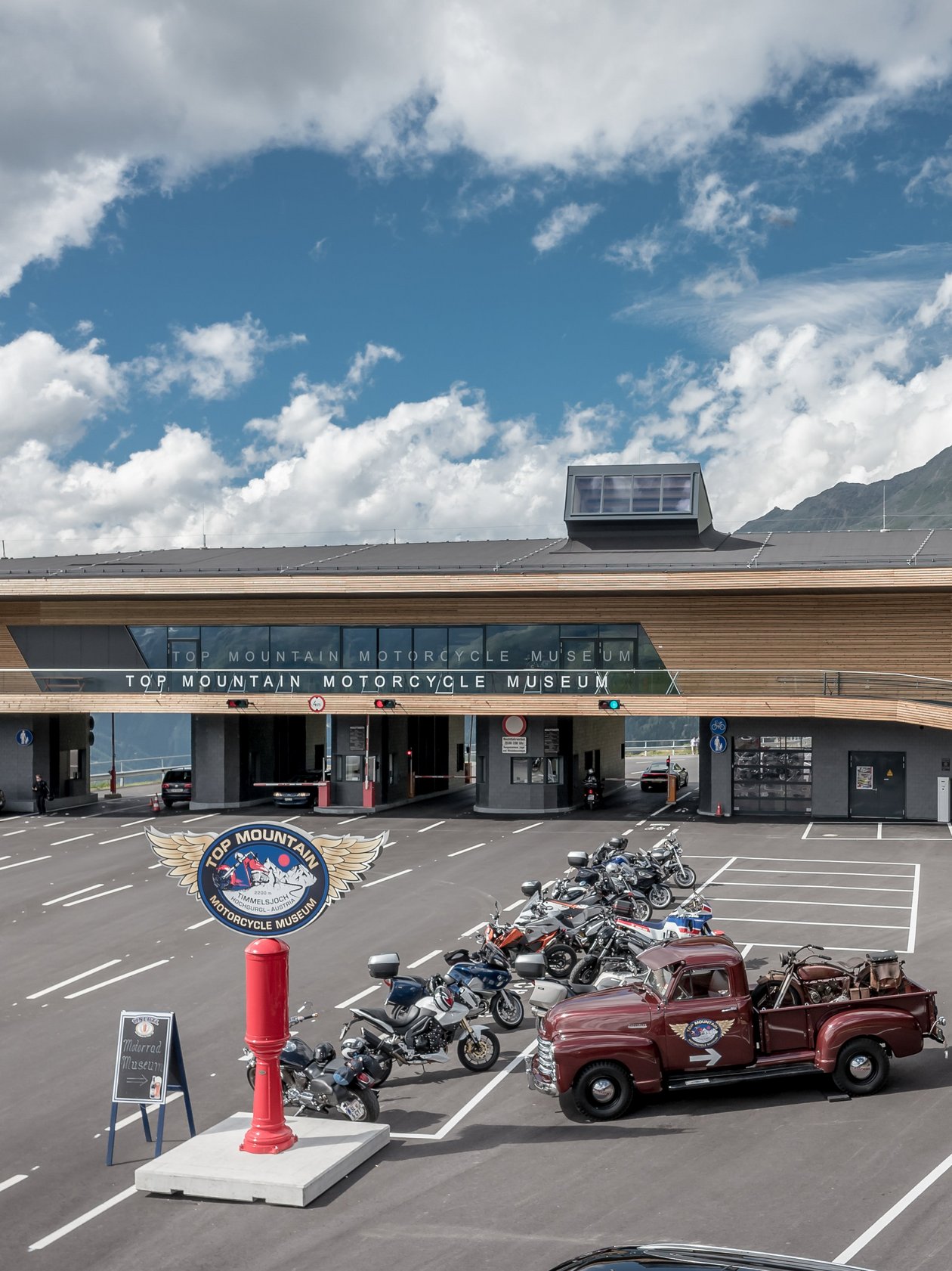 Außenansicht eines Motorradmuseums mit moderner Fassade und Motorradparkplatz in den Bergen