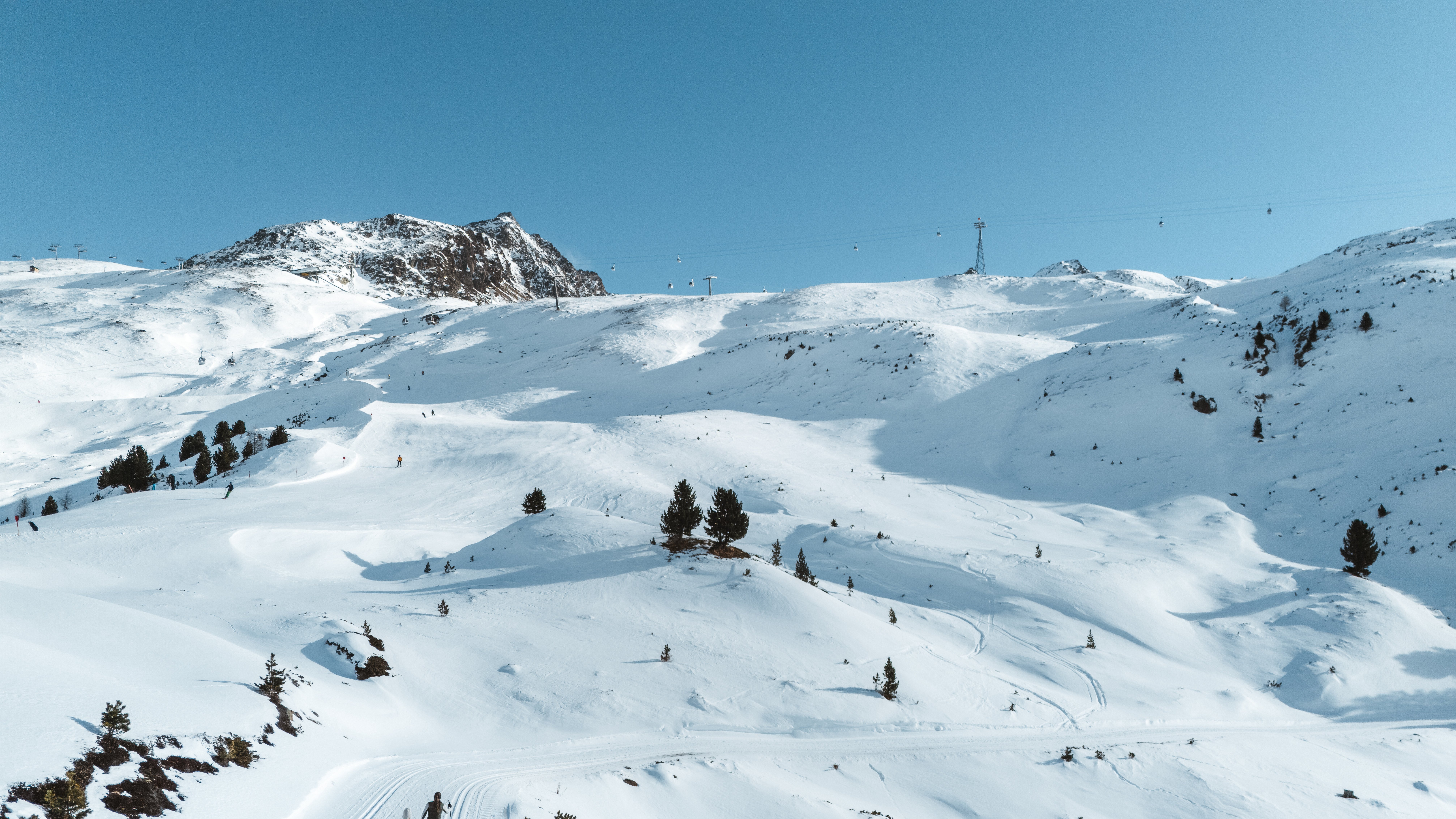 Verschneite Wanderwege im Hochgebirge Zwei Personen gehen auf einem verschneiten Wanderweg in den Bergen unter klarem Himmel.