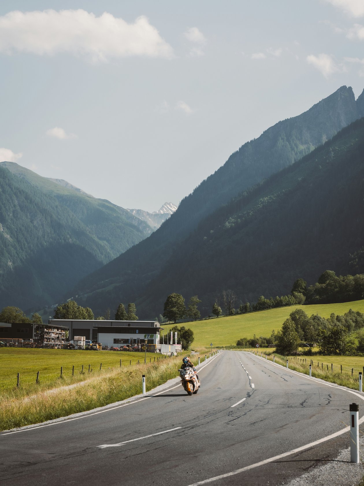 Motorradabenteuer in den Bergen Motorrad fährt auf einer kurvenreichen Straße mit Bergen im Hintergrund und grünem Landschaftsbild.