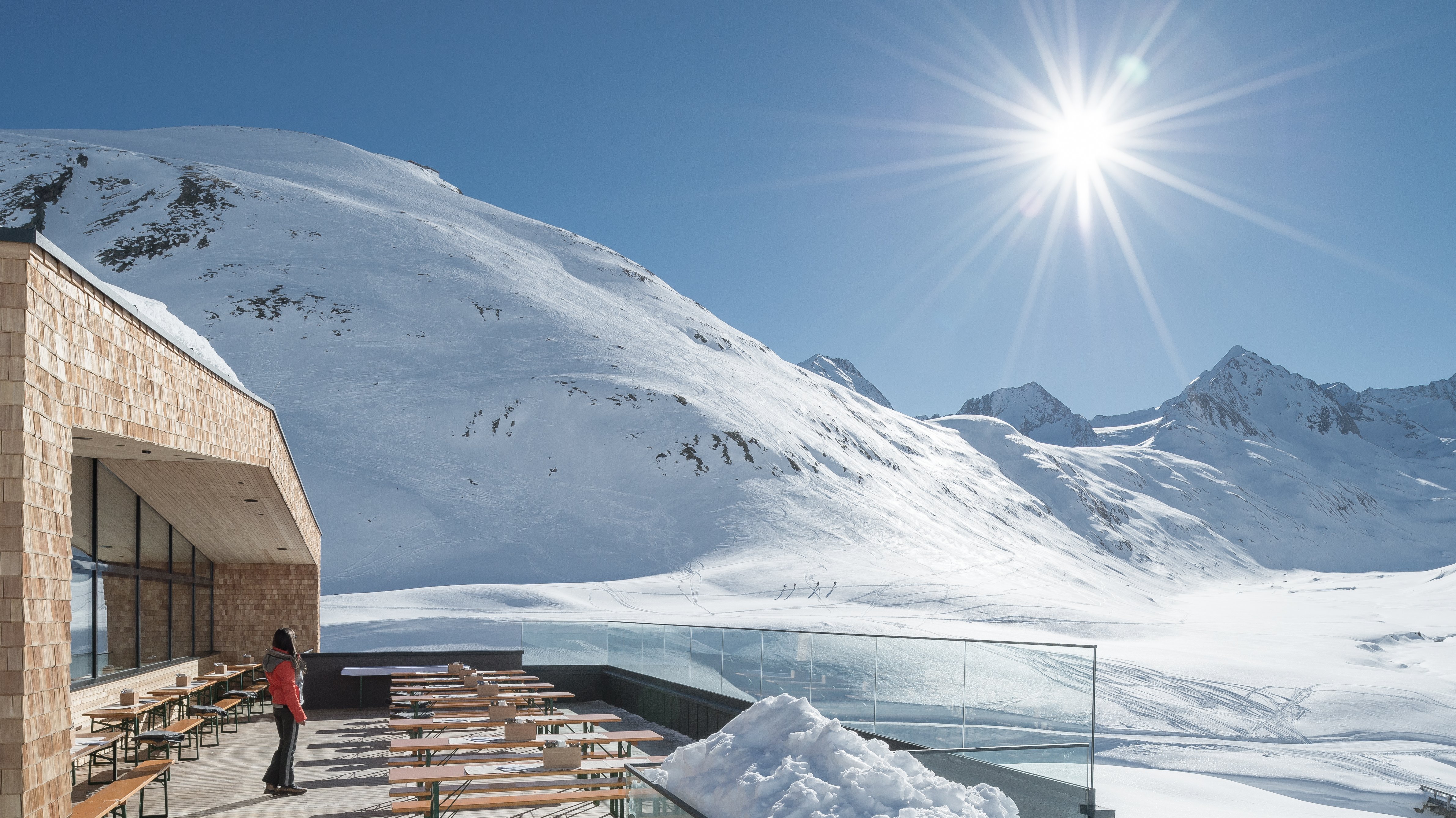 Modernes Gebäude mit Außenbereich und Blick auf schneebedeckte Berge unter blauem Himmel.