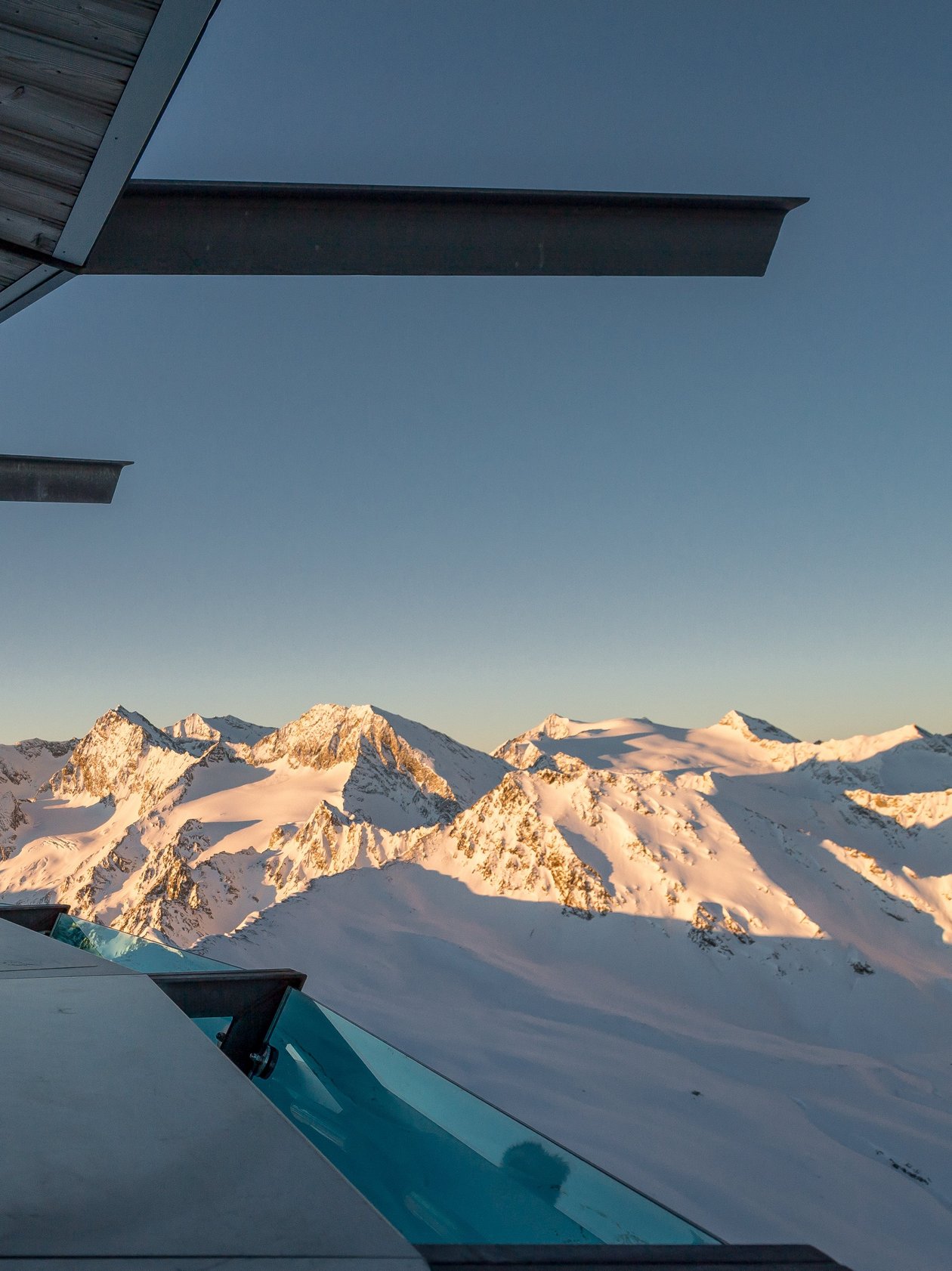 Bergblick bei Sonnenuntergang Zwei Personen stehen auf einer Aussichtsplattform mit Blick auf schneebedeckte Berge im Winter.